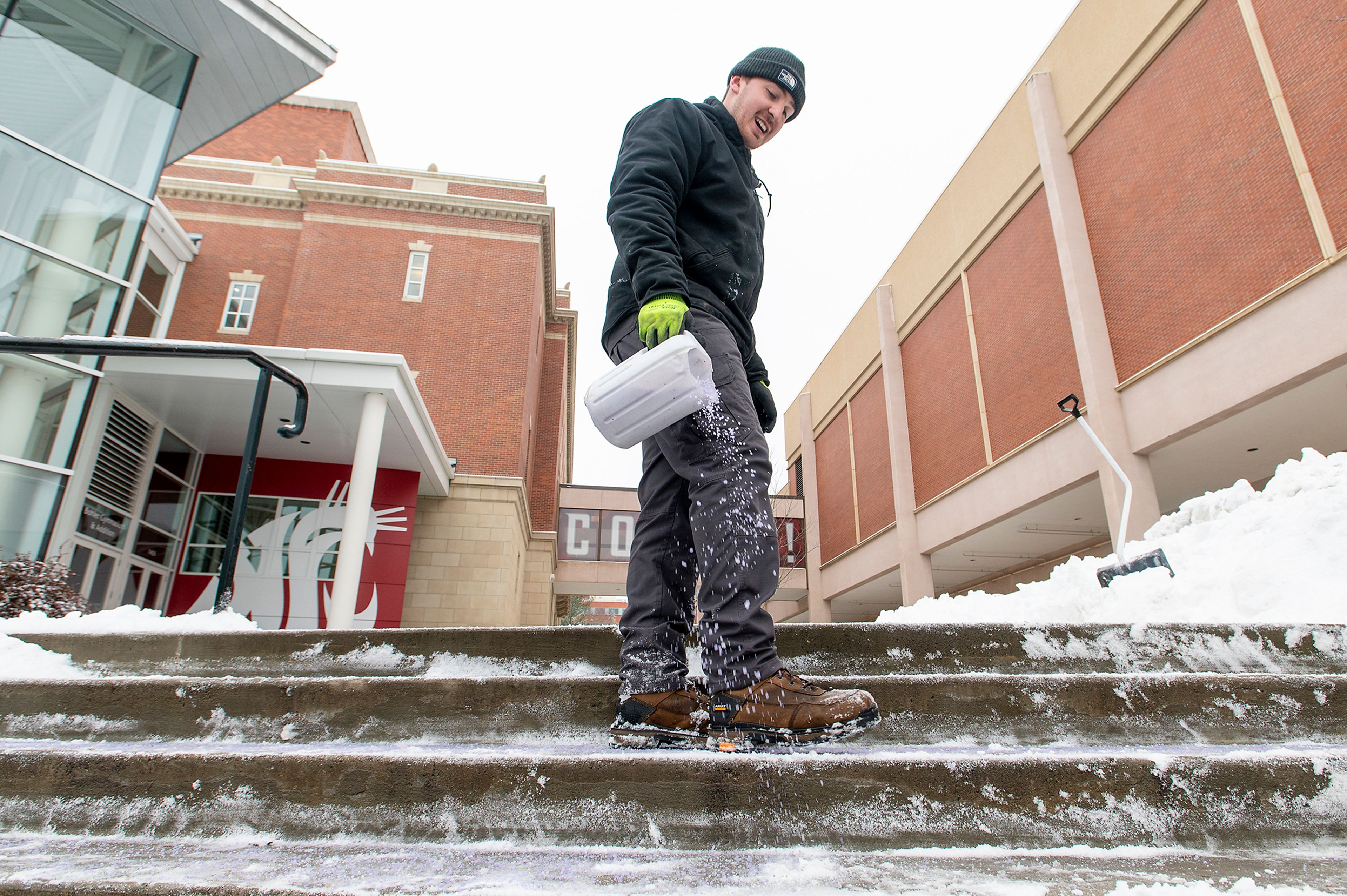 Brady Miller, of Washington State University’s grounds crew, sprinkles de-icer on a set of campus stairs in Pullman on Monday.