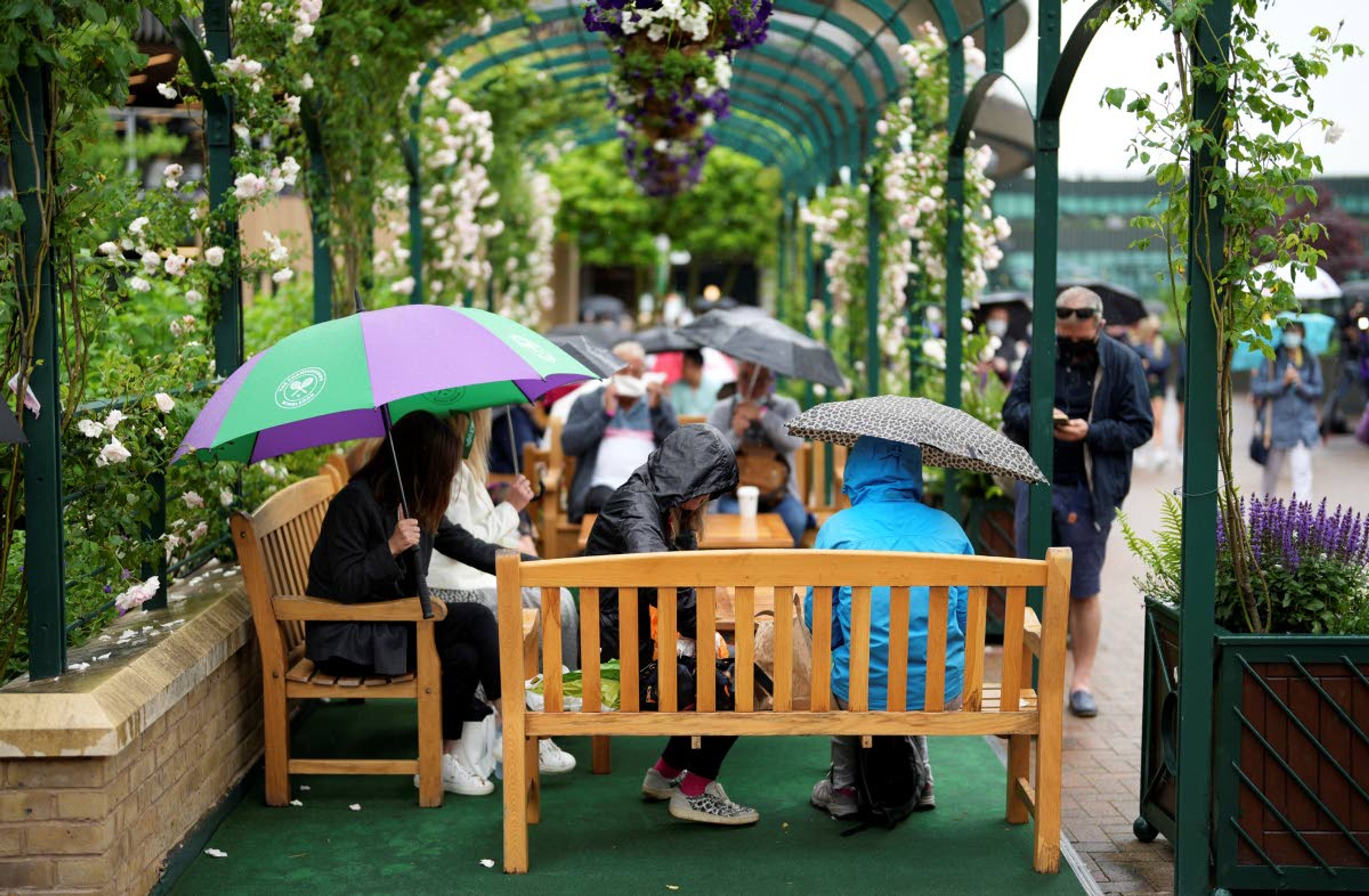 Spectators shelter under umbrellas during a rain delay on day one of the Wimbledon Tennis Championships in London, Monday June 28, 2021. (AP Photo/Alberto Pezzali)