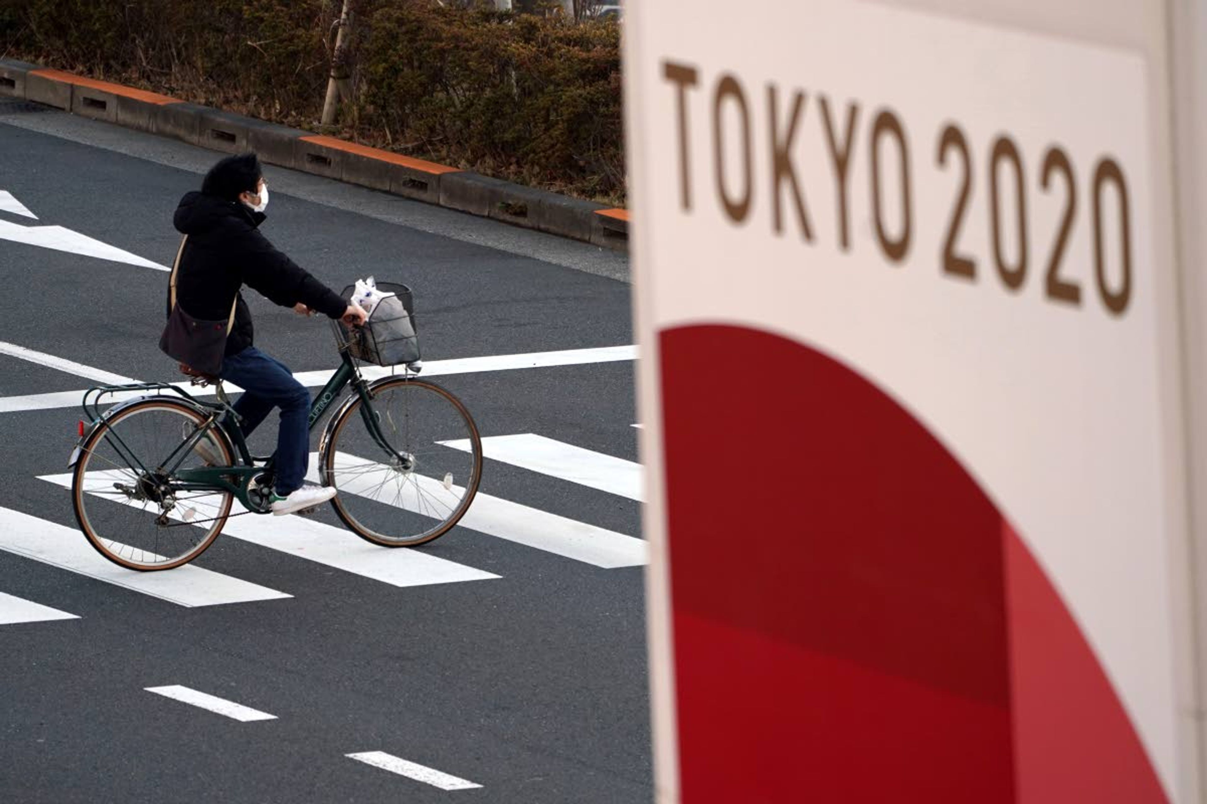 FILE - In this Jan. 21, 2021, file photo, a man wearing a protective mask to help curb the spread of the coronavirus rides a bicycle near a banner of the Tokyo 2020 Olympics in Tokyo. IOC officials say the Tokyo Olympics will open on July 23 and almost nothing now can stop the games from going forward. (AP Photo/Eugene Hoshiko, File)