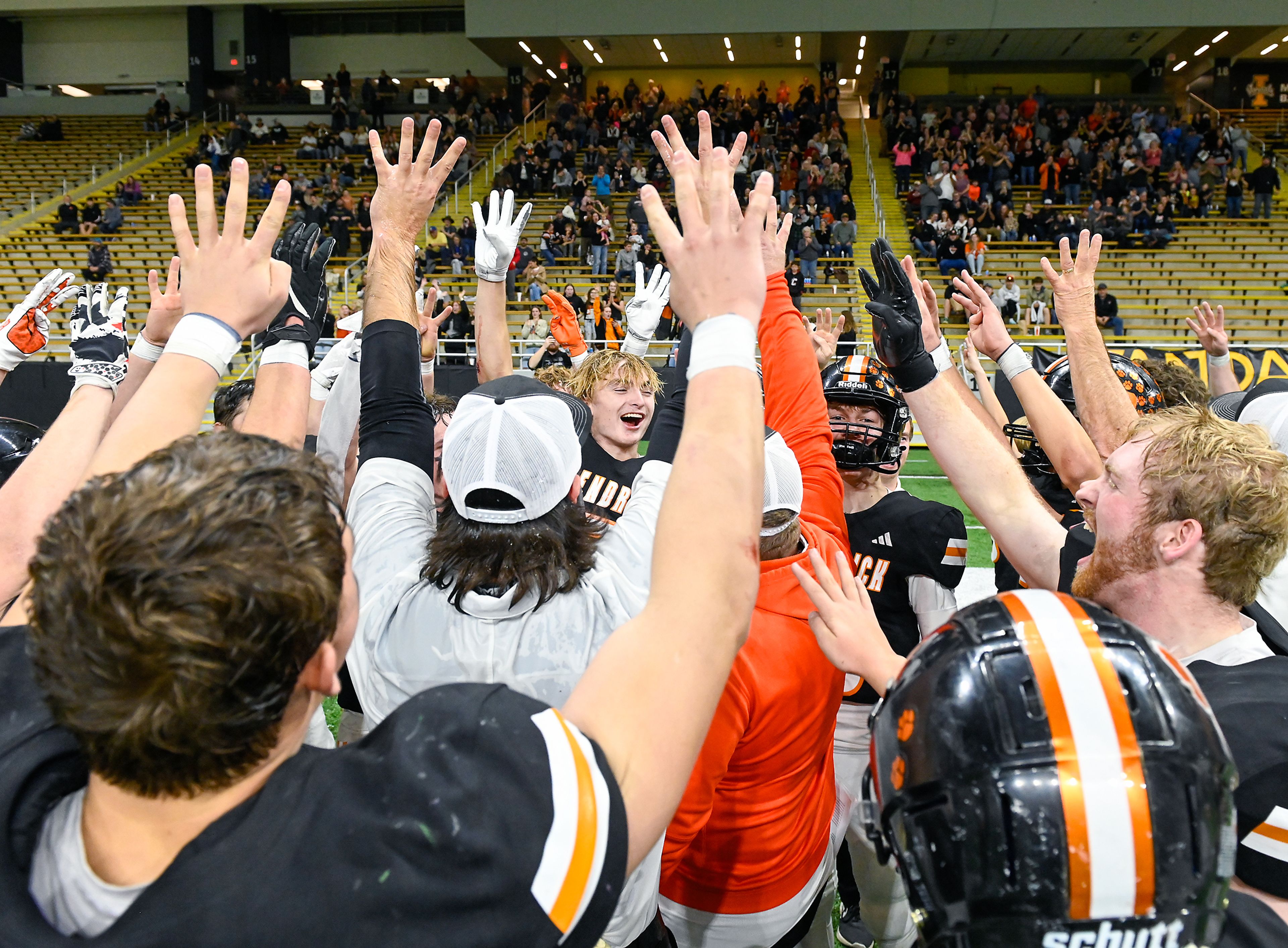 Kendrick players and coaches raise their hands with four fingers up, celebrating their fourth straight state championship — their first at Idaho Class 2A level after three at the 1A DII level — Friday after their win over Butte County at the P1FCU Kibbie Dome in Moscow.