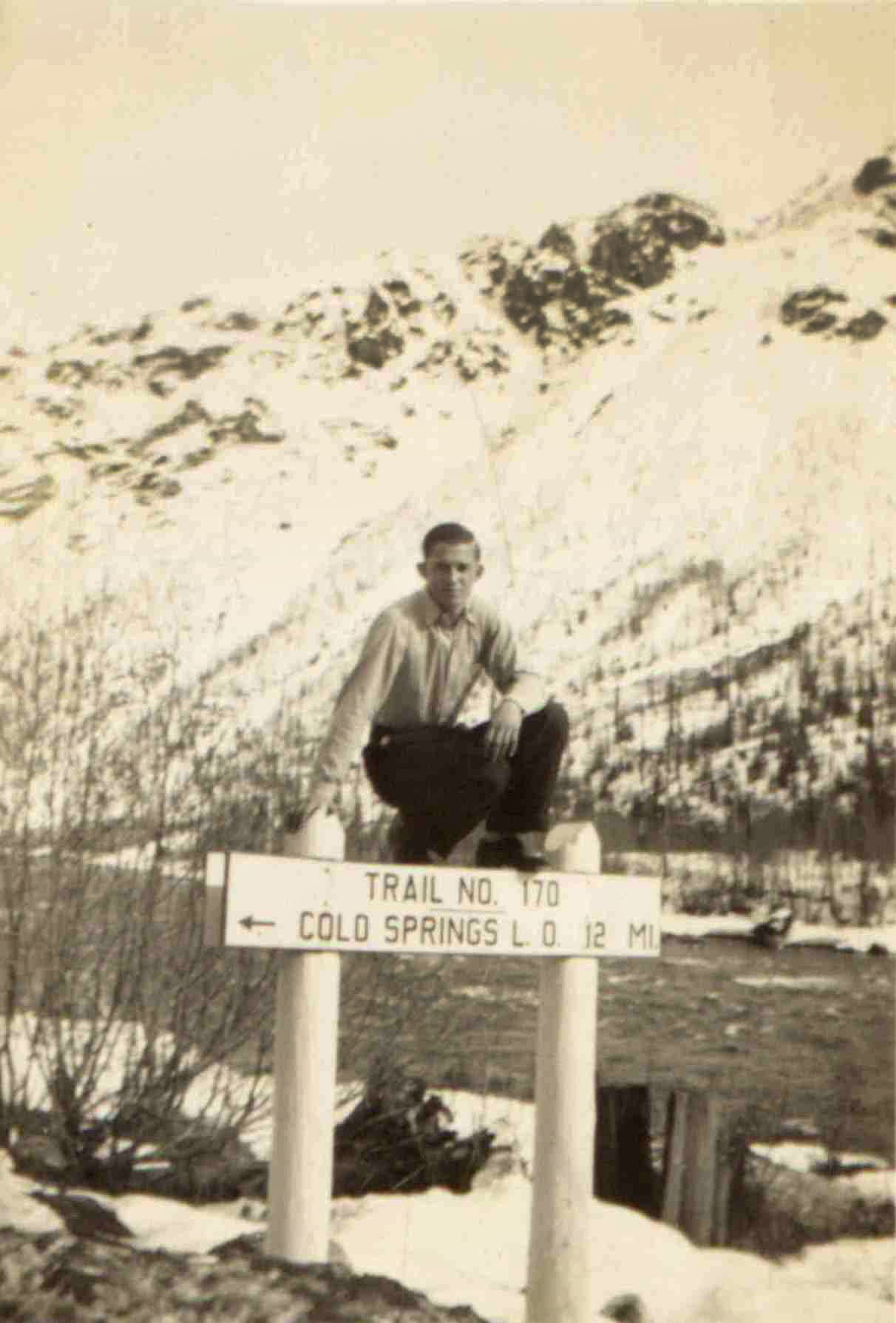 A friend of Arnold Sherwood Bates is seen on trail sign at Camp F-123, near Pierce. The photo is part of the Arnold Sherwood Bates photograph collection in the Univeristy of Idaho Library Special Collections and Archives.