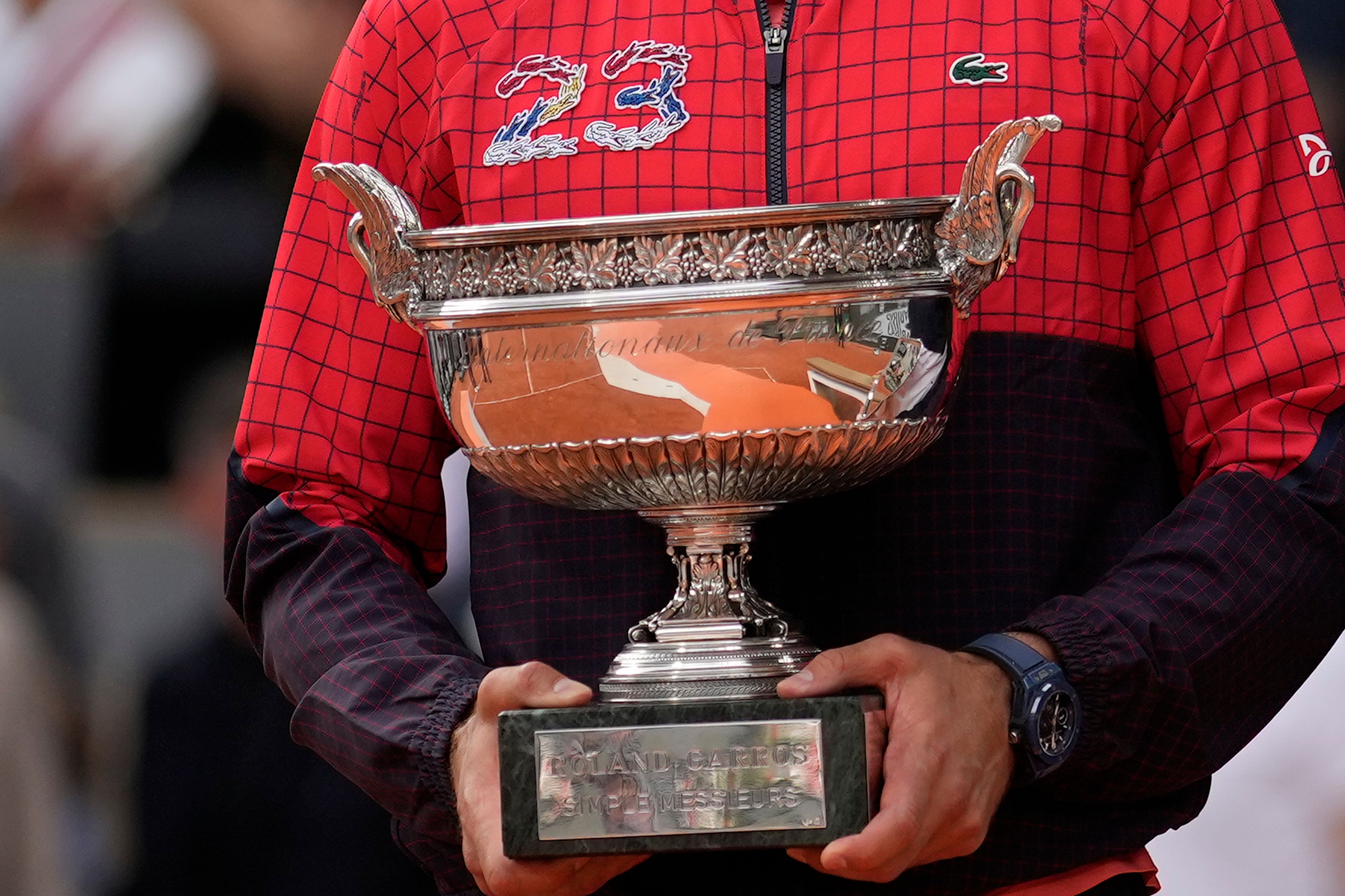 Serbia's Novak Djokovic, wearing a jacket with the number 23 for his 23rd Grand Slam final win, holds the trophy as he celebrates winning the men's singles final match of the French Open tennis tournament against Norway's Casper Ruud in three sets, 7-6, (7-1), 6-3, 7-5, at the Roland Garros stadium in Paris, Sunday, June 11, 2023. Djokovic won his record 23rd Grand Slam singles title, breaking a tie with Rafael Nadal for the most by a man. (AP Photo/Thibault Camus)