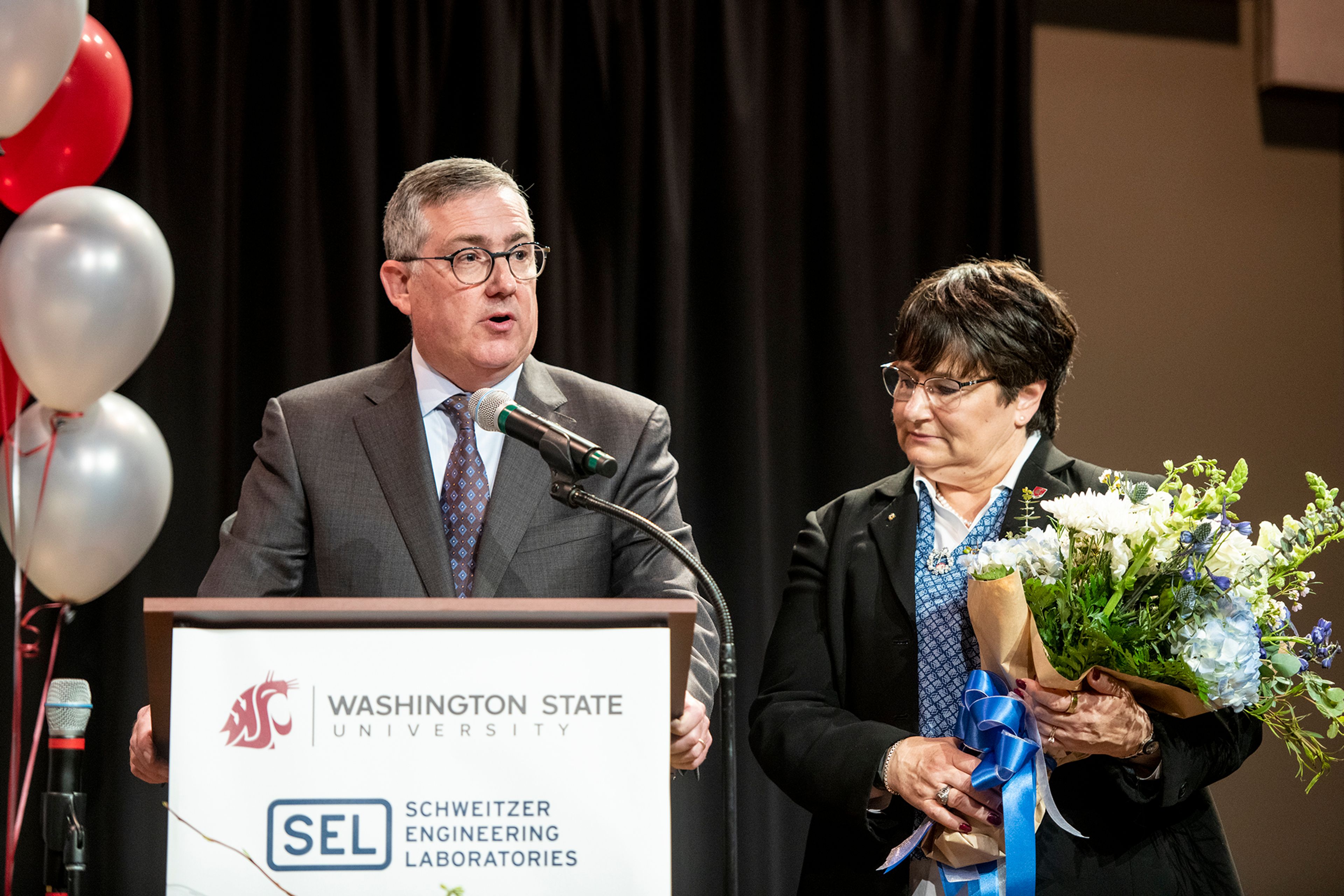 Washington State University President Kirk Schulz stands beside his wife, Noel Schulz, as he speaks to the audience about the long-standing relationship of Schweitzer Engineering Laboratories and WSU.