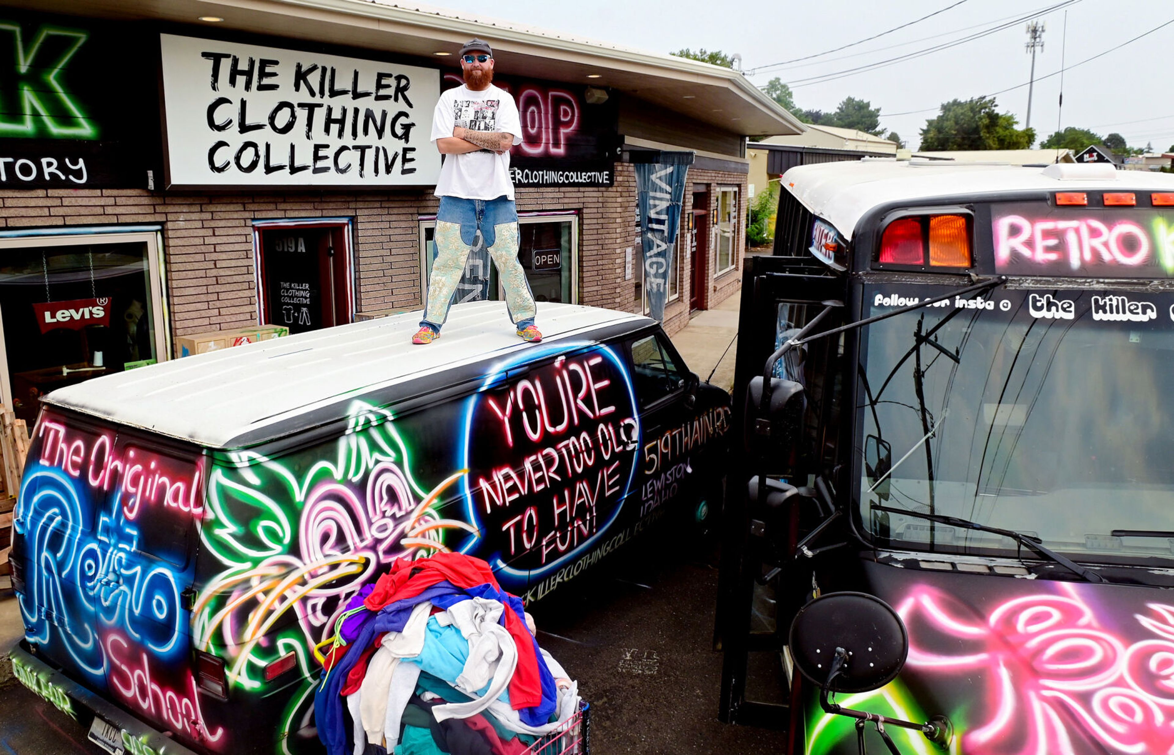 Patrick Brown-Hayes, owner and designer of The Killer Clothing Collective, on Monday stands on top of the collective’s van, raising him above the height of a bus also used for traveling to sites across Washington state to sell vintage, upcycled, and custom made clothing.