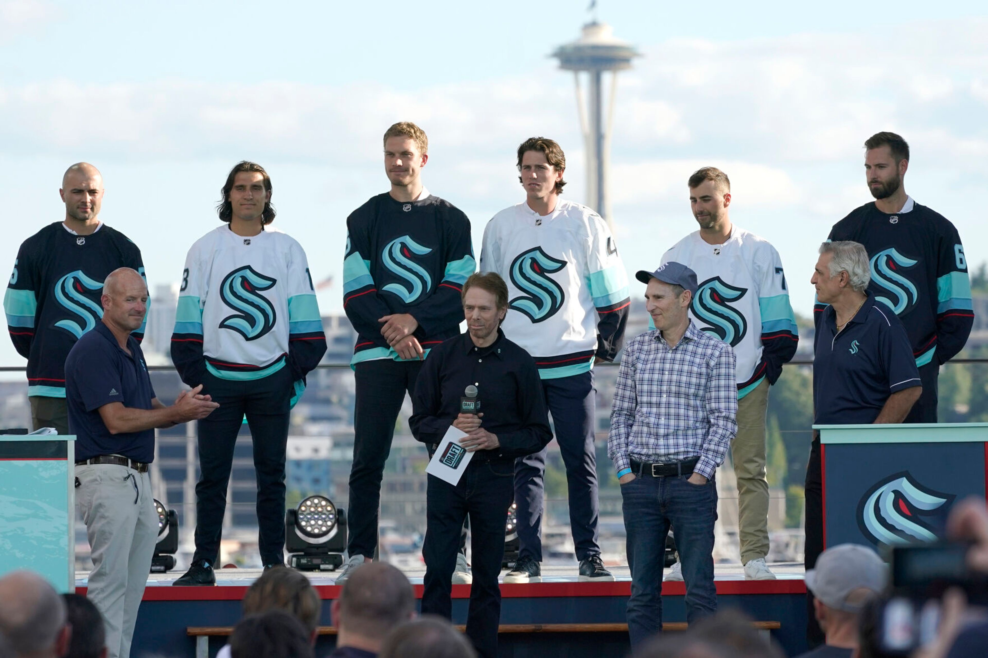 FILE - Seattle Kraken owners Jerry Bruckheimer, front center, is joined by owners David Wright, front left, and Andy Jassy, front second from right, with Kraken general manager Ron Francis, front right, and new Seattle Kraken NHL hockey players, back row from left, Mark Giordano, Brandon Tanev, Jamie Oleksiak, Hadyn Fluery, Jordan Eberle and Chris Dreidger, Wednesday, July 21, 2021, after being introduced during the Kraken's expansion draft event in Seattle. With Hollywood filmmaker Jerry Bruckheimer as part of the ownership group, the Seattle Kraken were always going to have a big cinematic element to any video production the team produced. (AP Photo/Ted S. Warren, File)