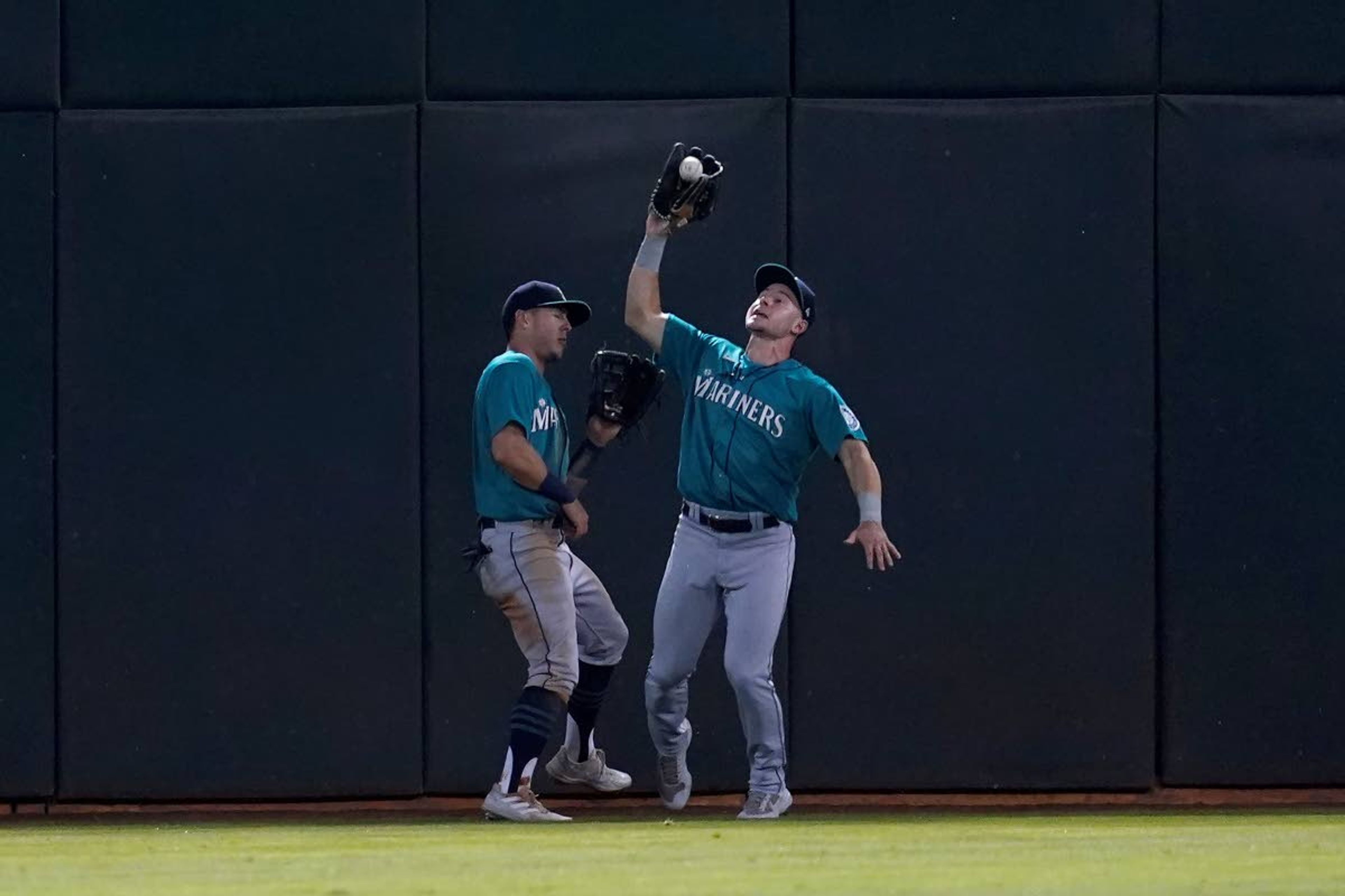 Seattle Mariners center fielder Jarred Kelenic, right, catches a flyout hit by Oakland Athletics' Yan Gomes next to left fielder Dylan Moore during the fourth inning of a baseball game in Oakland, Calif., Monday, Sept. 20, 2021. (AP Photo/Jeff Chiu)