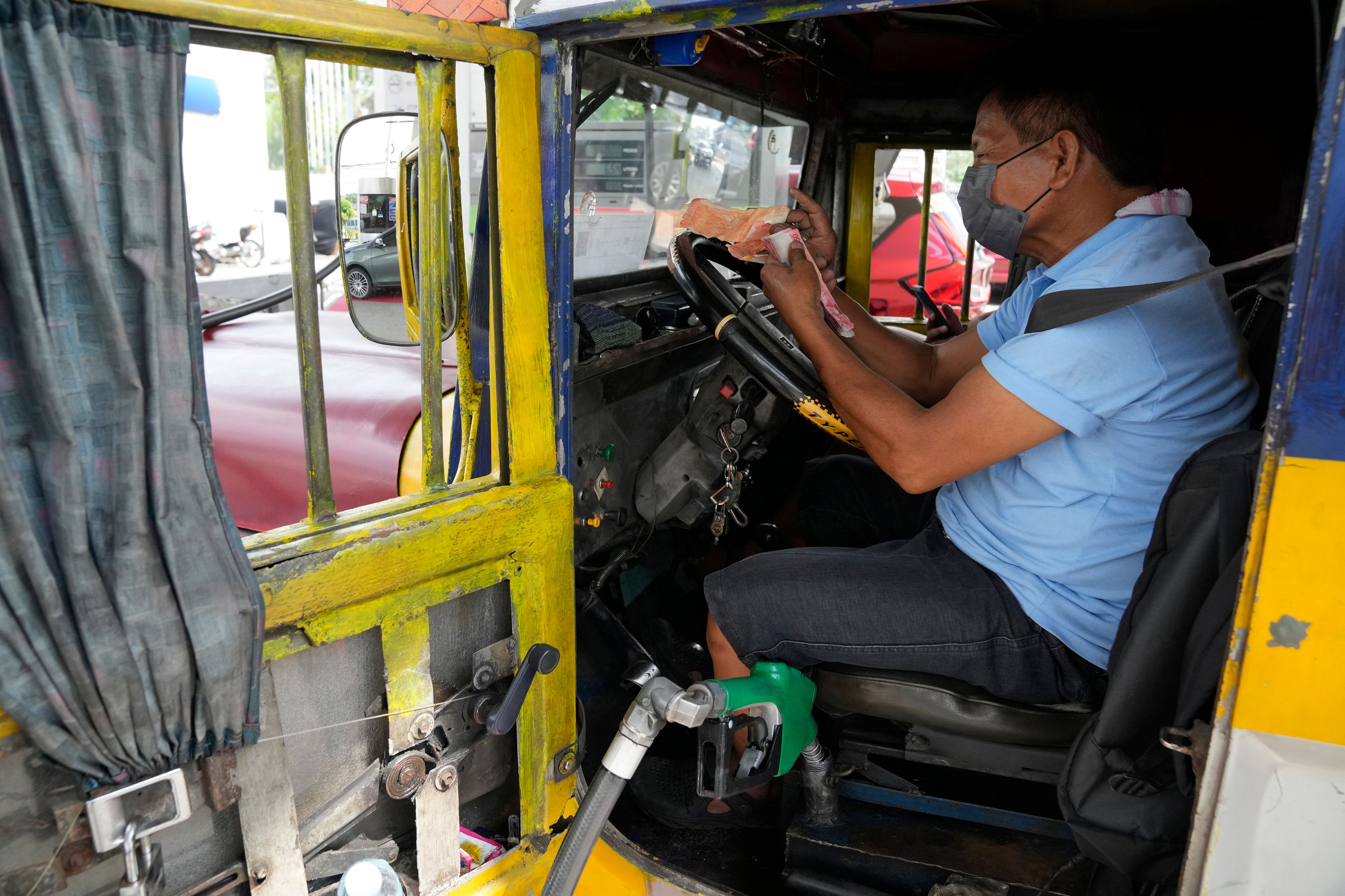 A passenger jeepney driver counts money from his earnings Monday, which he will use to refuel his vehicle at a gasoline station in Quezon City, Philippines.