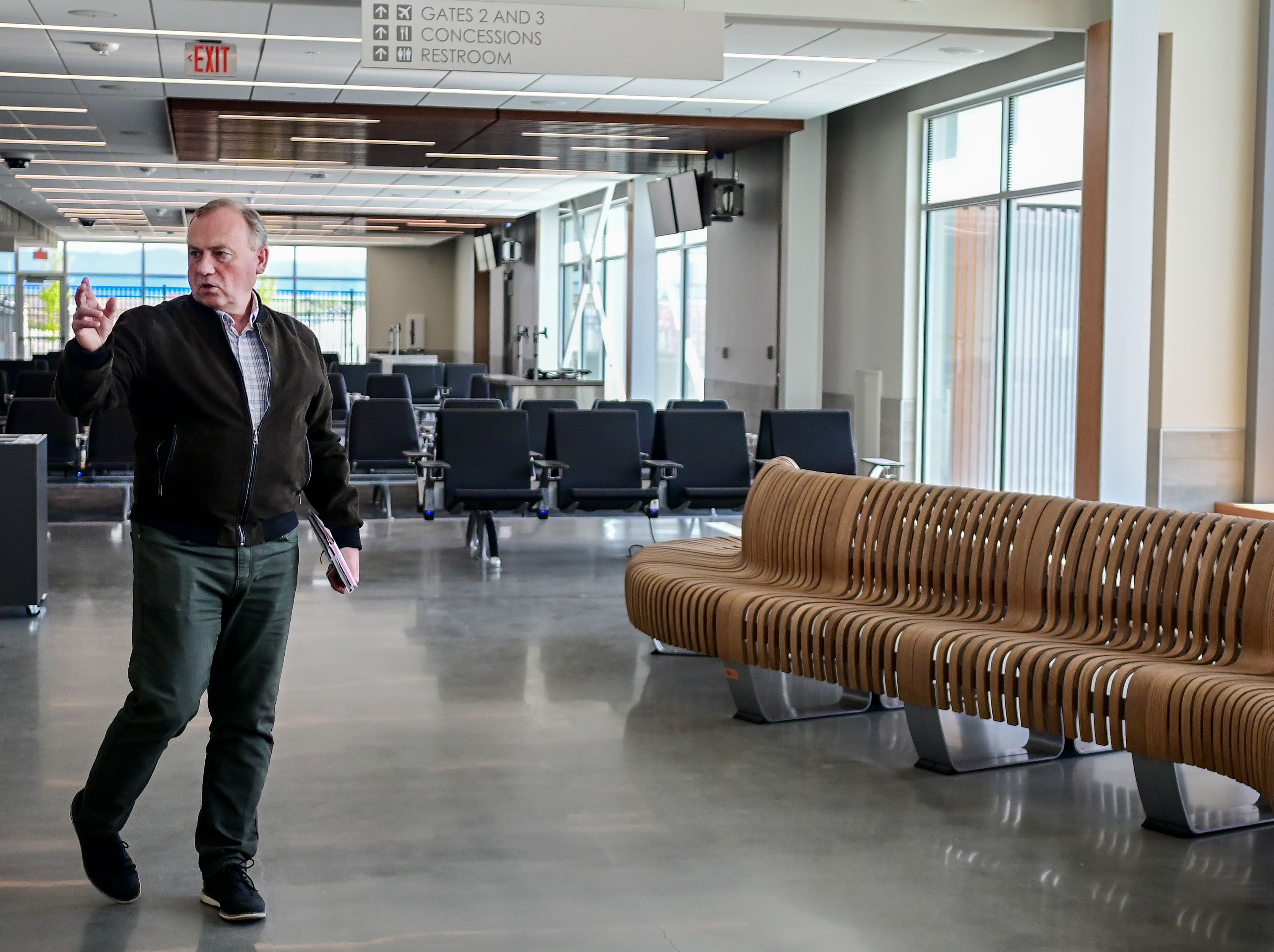 Pullman mayor Francis Benjamin points out different aspects of the new terminal at the Pullman-Moscow Regional Airport at Schweitzer Field during a media tour in Pullman on Tuesday. The terminal has three gates, with two to the left of the building (behind Benjamin) and a recomposure bench, right, for fliers to use following TSA screenings.