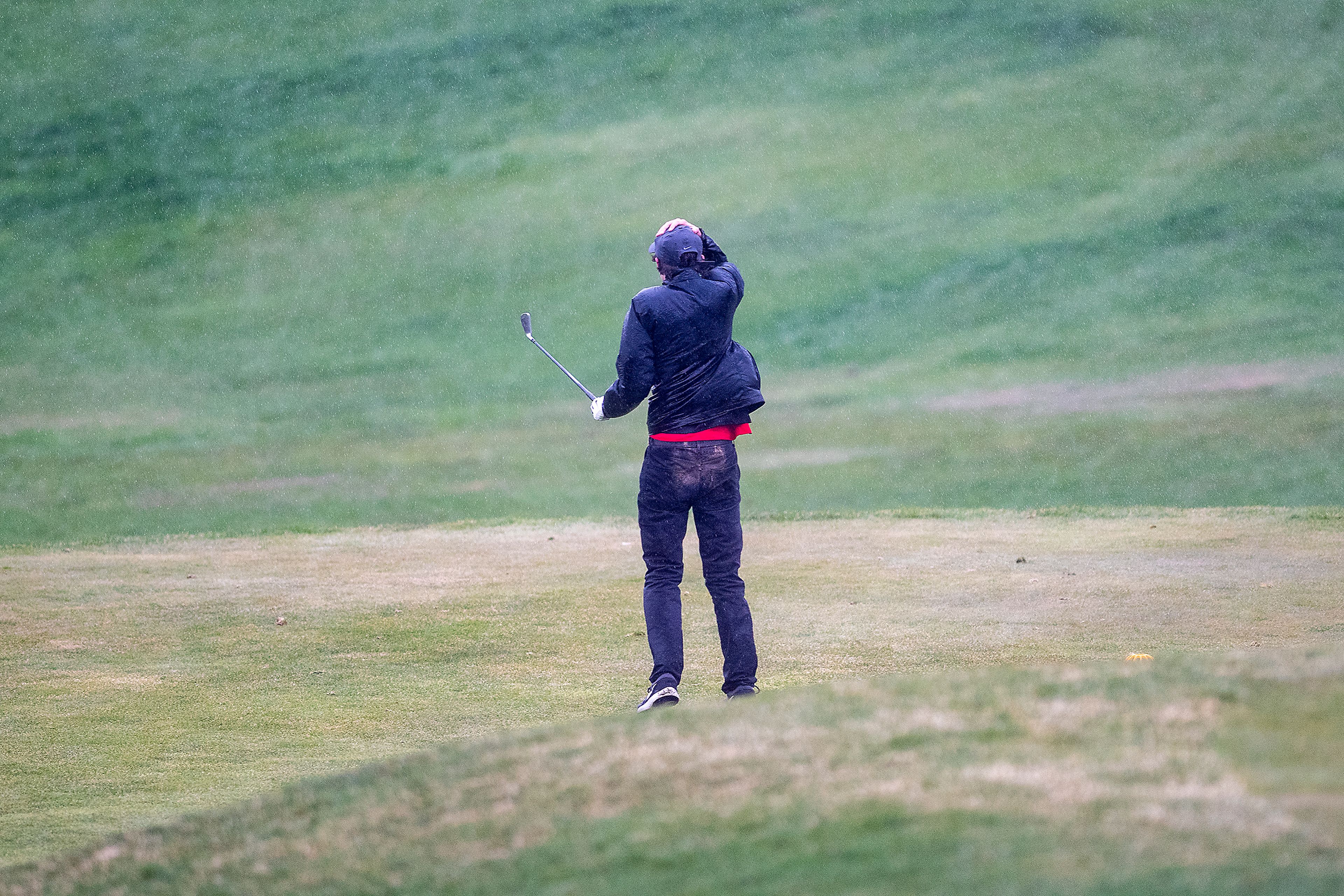 Zach Wilkinson/Daily News A man searches for his tee shot while holding his hat against high gusts of wind and heavy rainfall Monday while playing a round of golf at the University of Idaho golf course in Moscow.