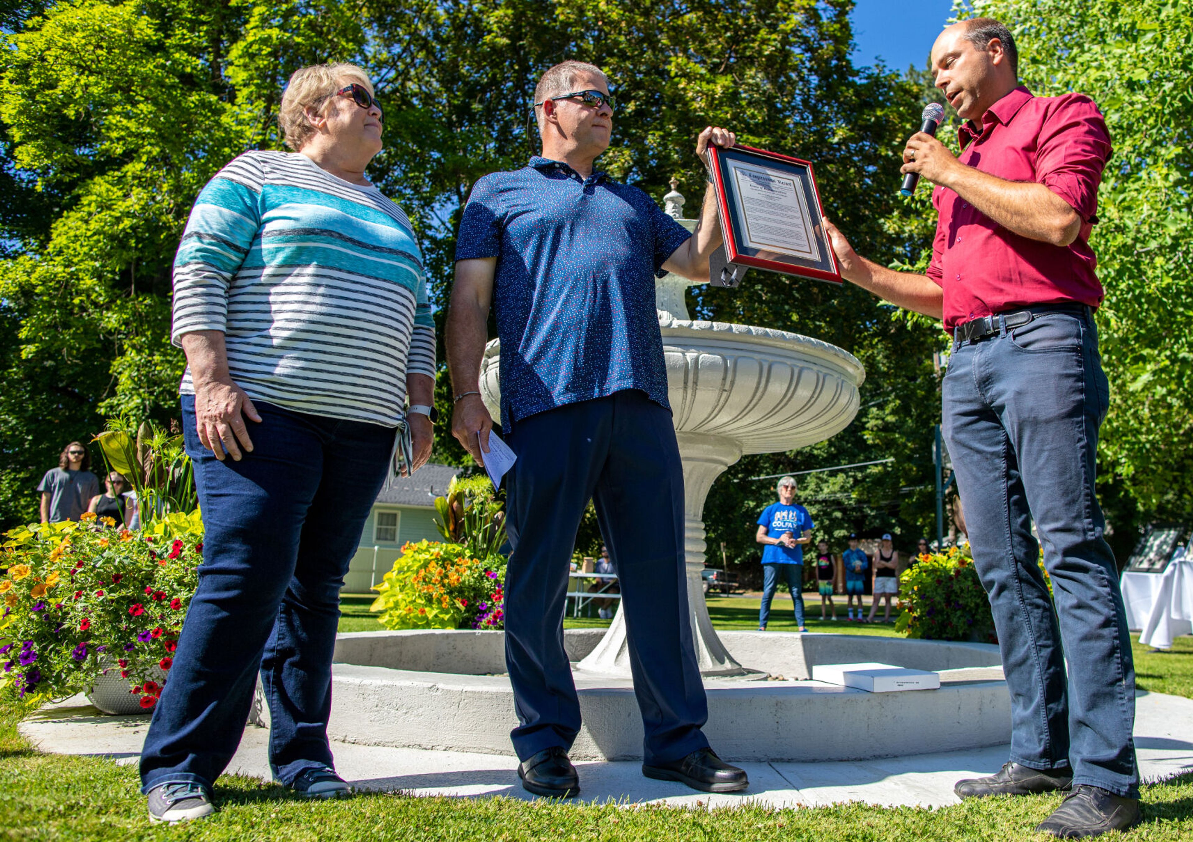 Andrew Engell, the deputy district director to State Representative Cathy McMorris Rogers, right, reads a letter of congressional record from Rogers honoring the rededication of Lippett Fountain at Eells Park in Colfax on Saturday with some help from the city’s Mayor James Retzer, center, during Colfax’s 150th birthday celebration.