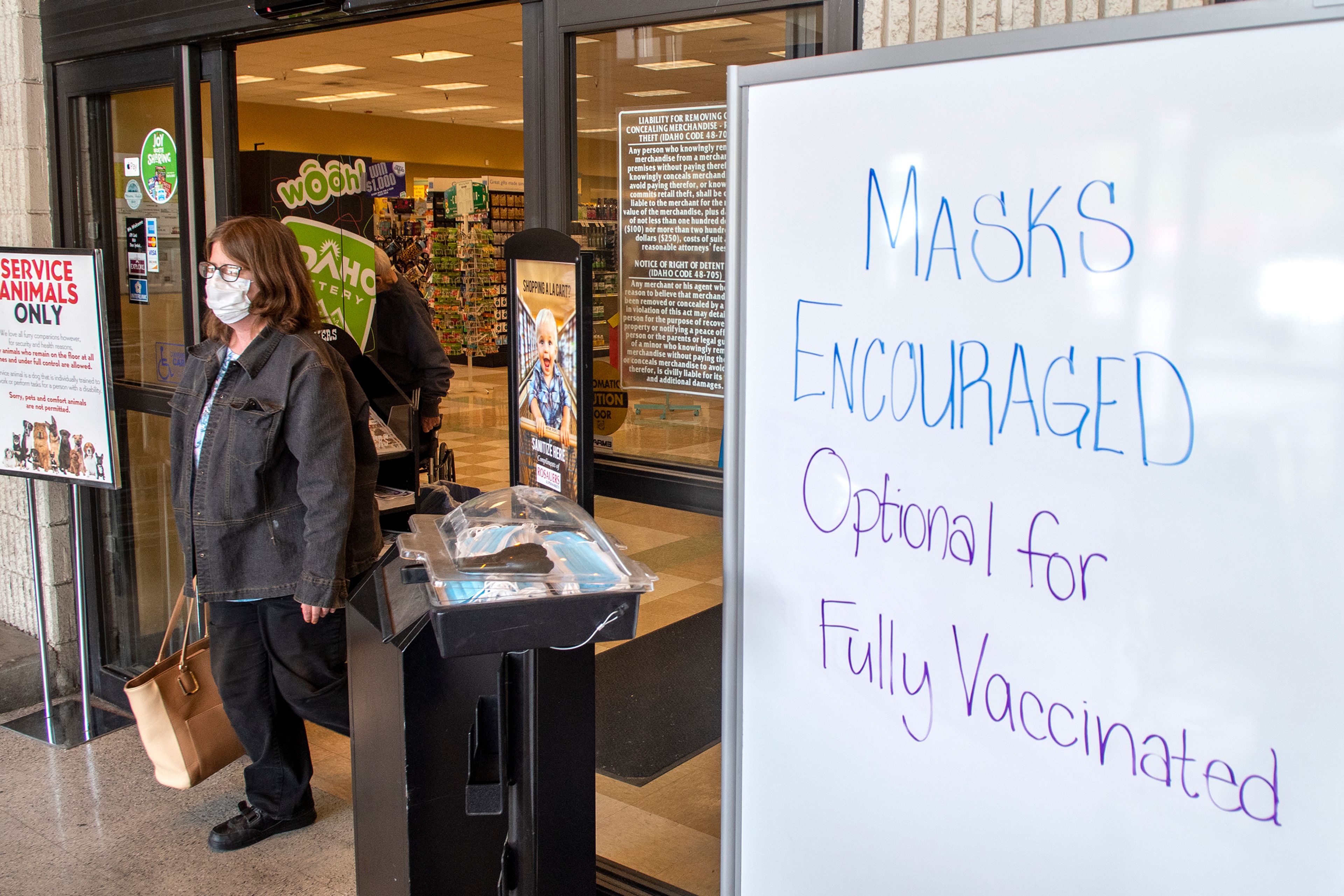 A masked woman exits Rosauers Supermarket off north Main Street in Moscow passing by an updated sign that encourages shoppers to wear masks the day after Moscow City Council lifted the town’s face mask order. Businesses can still require patrons to wear masks in their establishment.