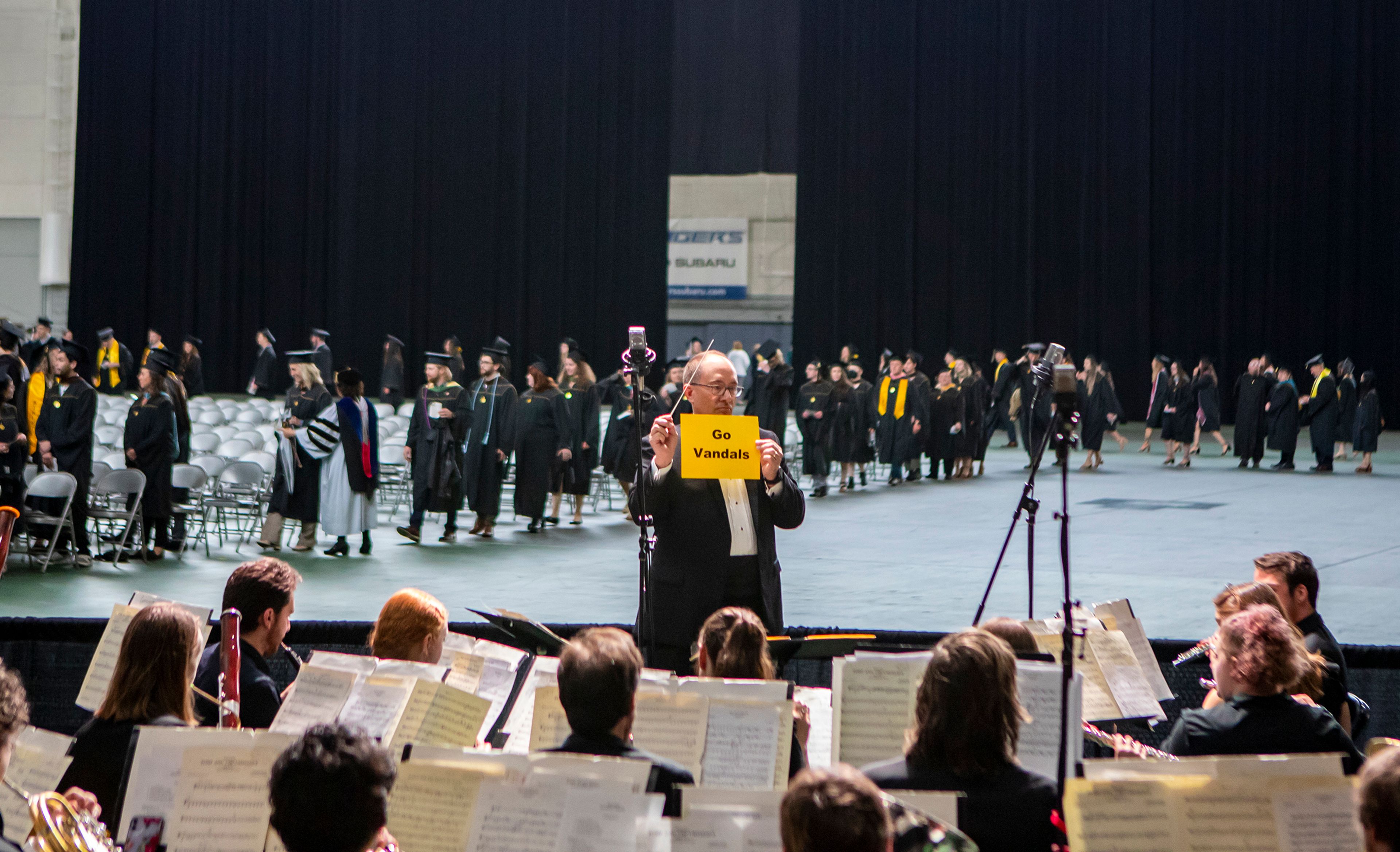 The conductor of the orchestra holds up a “Go Vandals” sign while leading his musicians as graduates take their seats Saturday morning during the University of Idaho’s 2022 Spring Commencement Ceremony at the Kibbie Dome in Moscow.