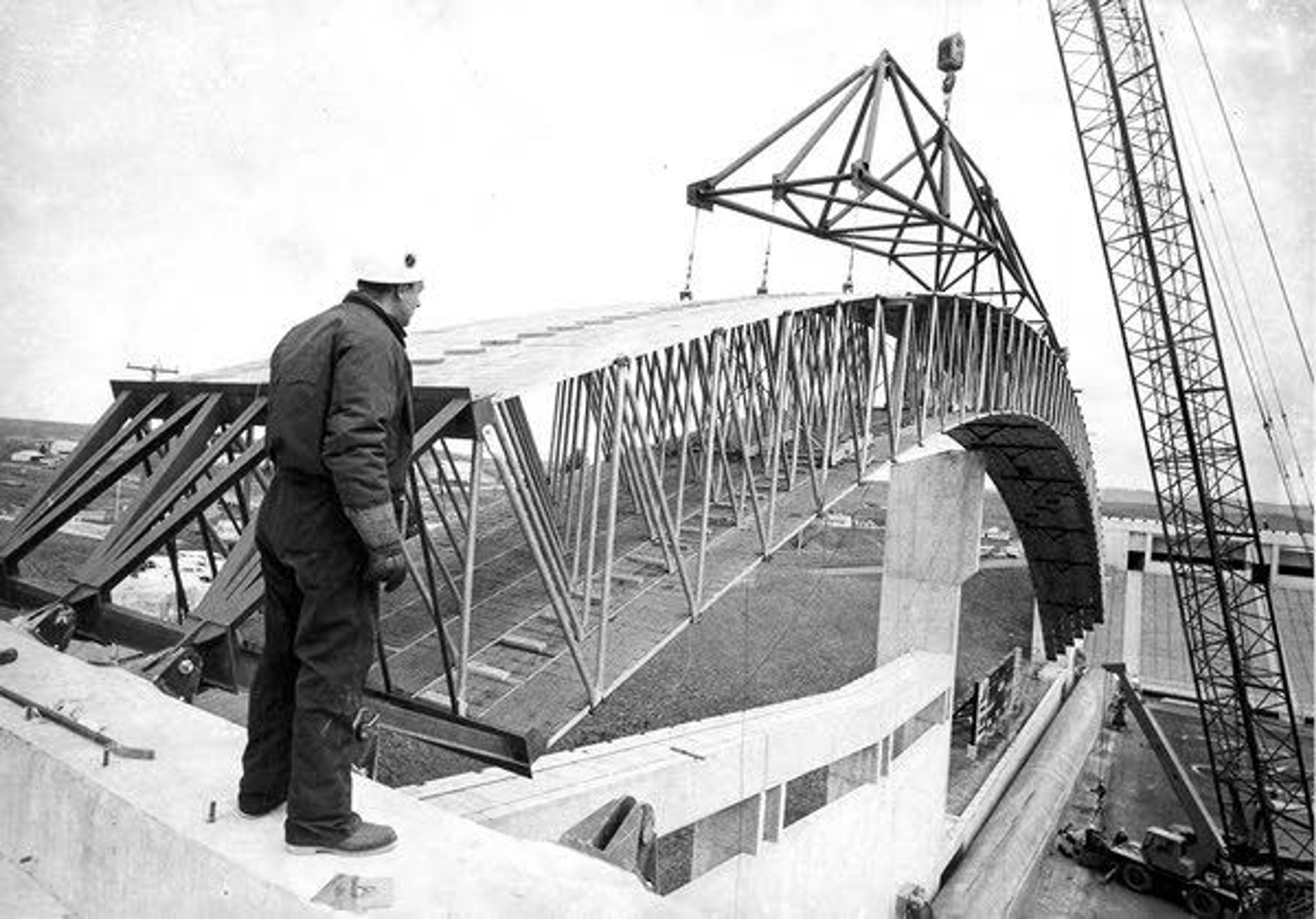 Above: A construction worker watches while a crane lifts the end of a roof beam into place during the construction of the roof of the ASUI Kibbie Activity Center in Moscow in 1975. Below: A view of the roof from a distance during construction.