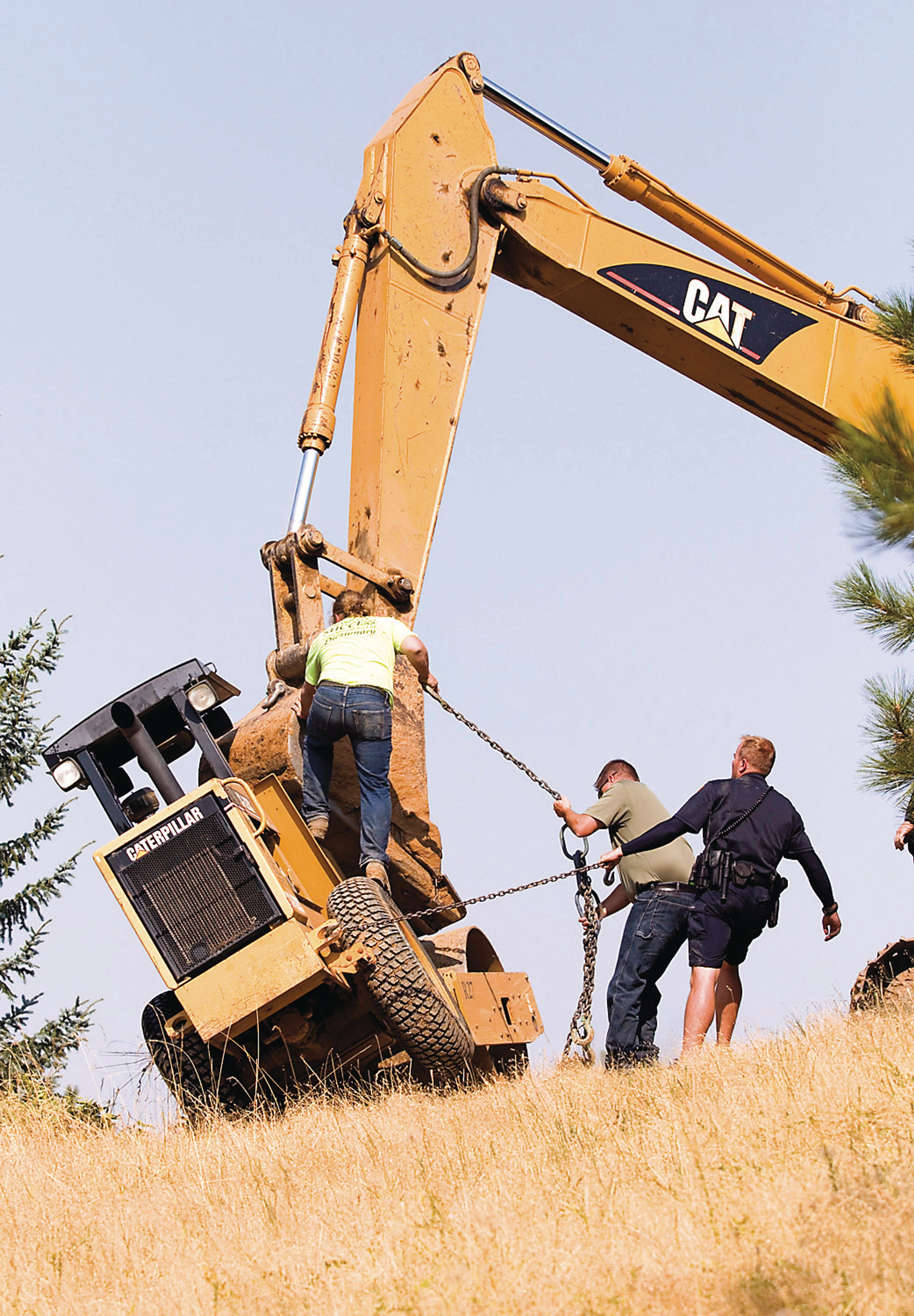 A construction worker and emergency responders use chains to secure a roller to an excavator to prevent it from tipping over next to the Vista Water Tank near Hathaway Street on Thursday in Moscow. The roller had accidentally tipped over, killing the driver who was and employee of Motley-Motley Inc.