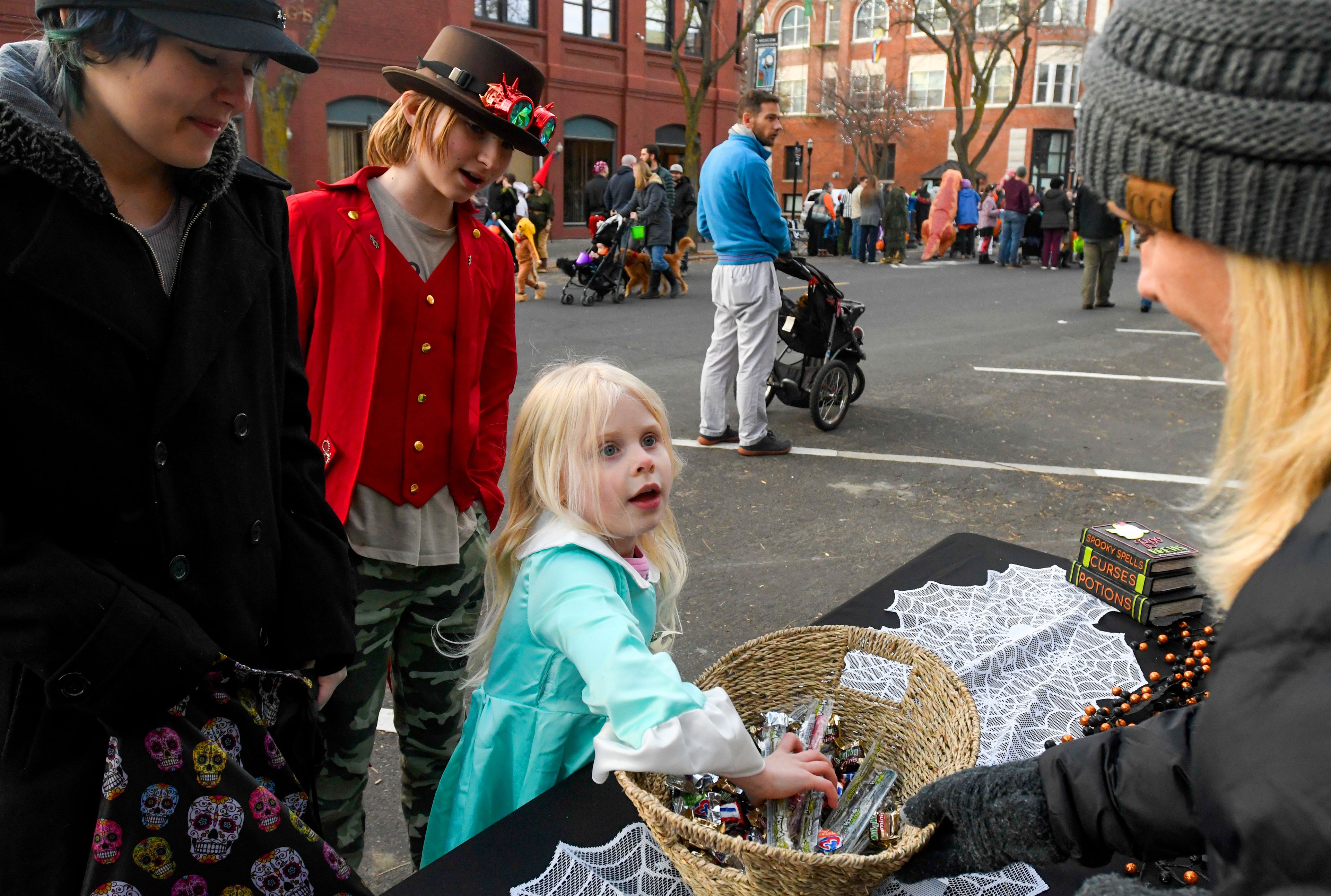 Ari Fish, left, 16, and Alex Fish, 13, laugh as Riley Davis, center, 5, looks up from digging in the candy basket to ask for gummy bears from Erika Odenborg, right, at the Latah Credit Union table set up at Moscow’s Downtown Trick-or-Treat on Tuesday.