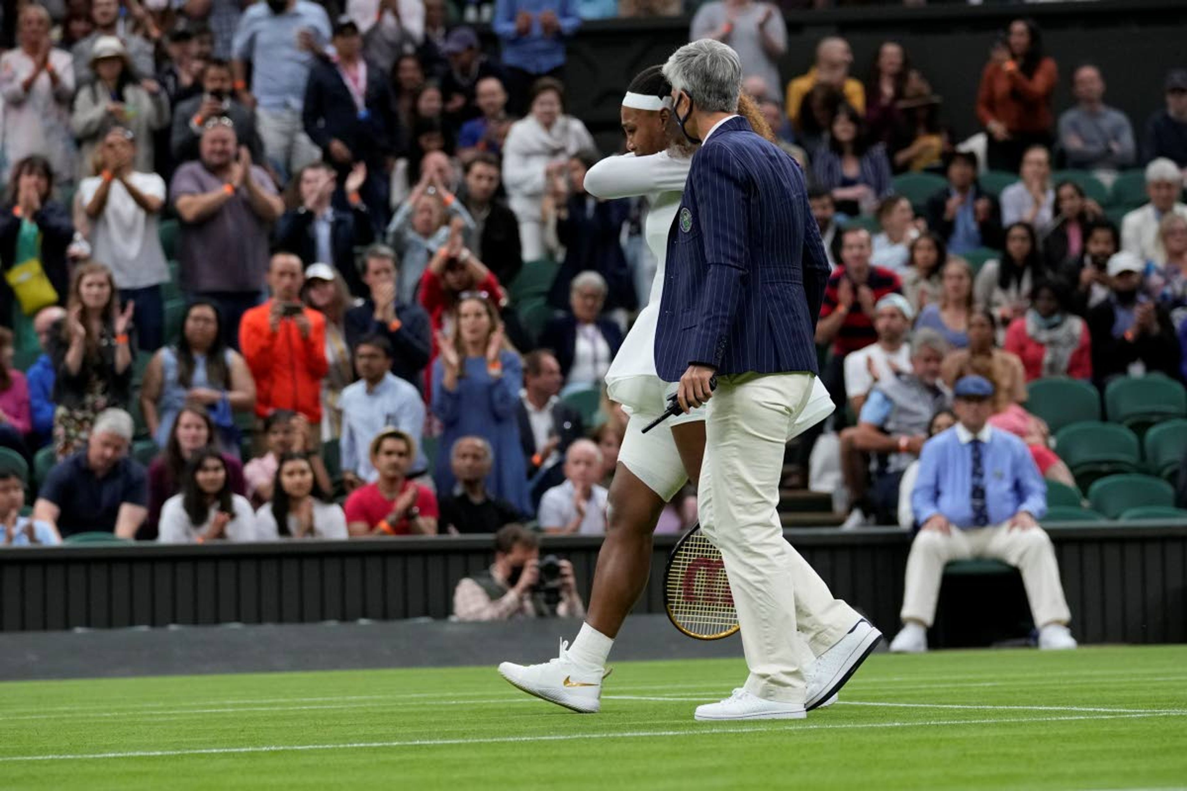 A referee helps Serena Williams of the US off the court after retiring from the women's singles first round match against Aliaksandra Sasnovich of Belarus on day two of the Wimbledon Tennis Championships in London, Tuesday June 29, 2021. (AP Photo/Kirsty Wigglesworth)