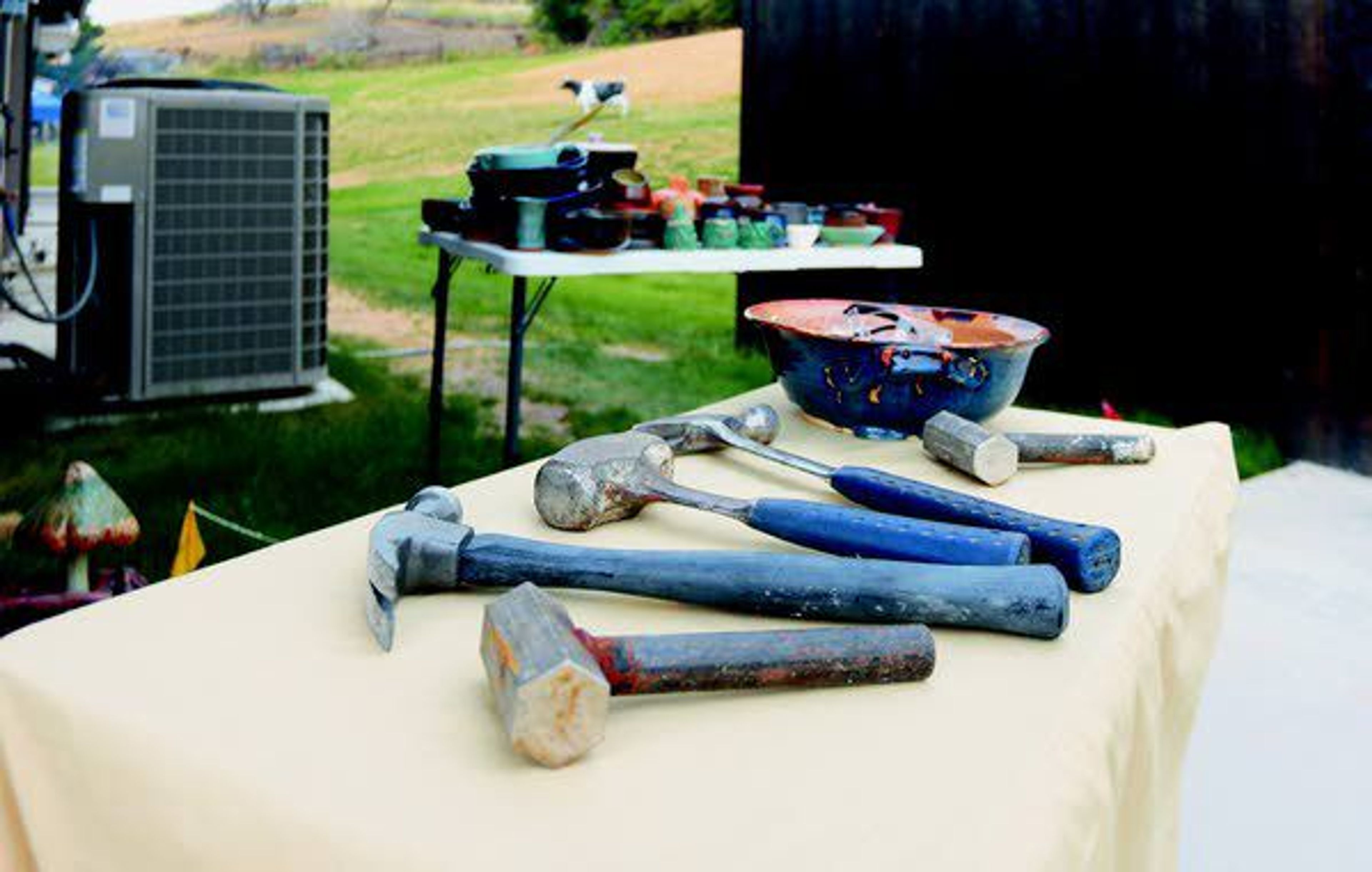 Hammers and safety glasses sit on a table, waiting to smash a tableful of pottery in the background. For a dollar, kiln shed fundraiser attendees at the Dahmen Barn could smash the pottery of their choice, or for $5 they could take it home.