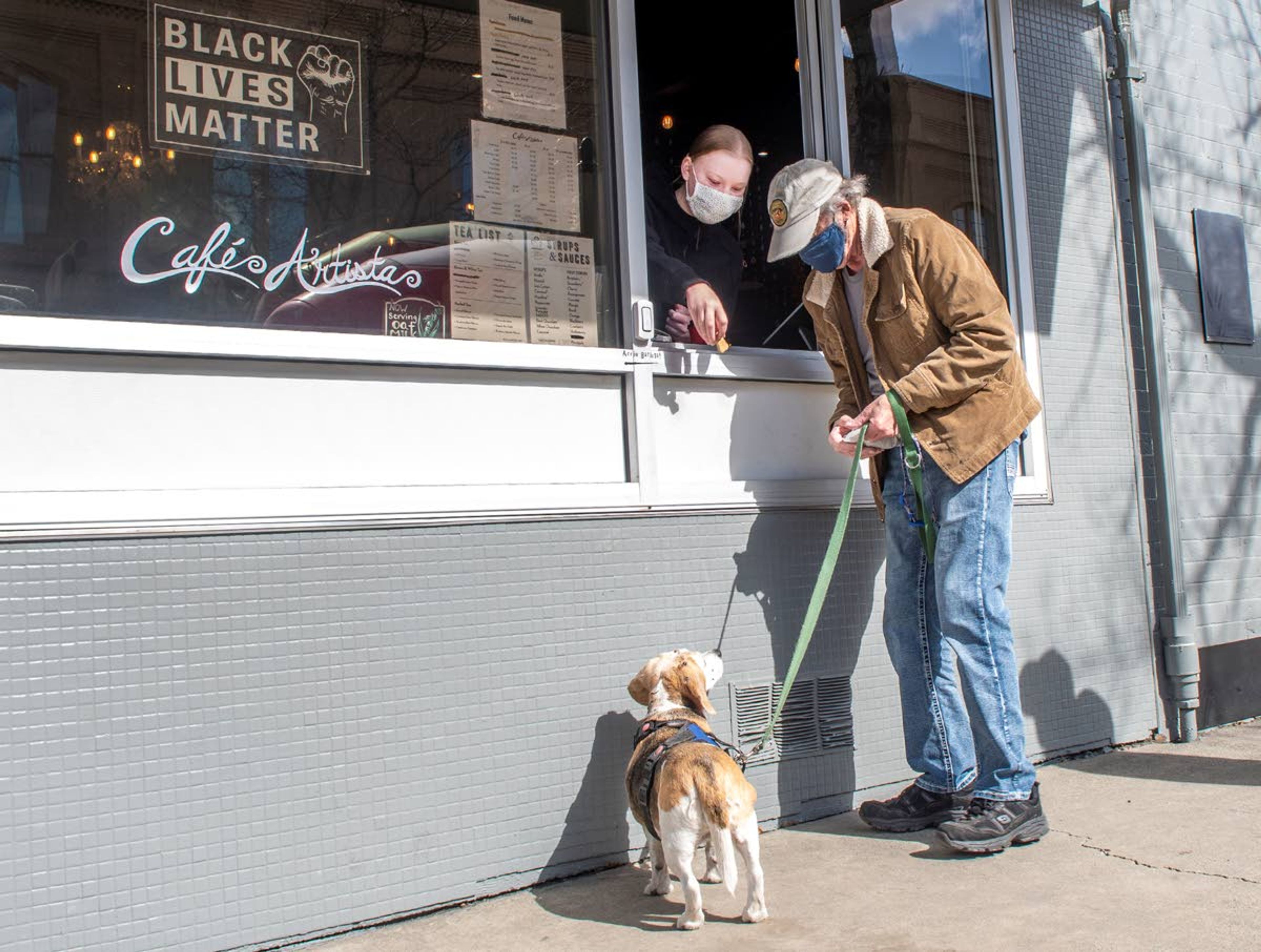 Daisy, a 15-year-old beagle, waits next to her owner, Wayne Christensen, as barista Eva Woods reaches out a walk-up window with a dog treat at Cafe Artista in Moscow on Tuesday morning. “I’ve been coming here every day for three years. The people are nice and quick. I couldn’t go in, so without the window, I would have had to find a new place to go,” Christensen said.