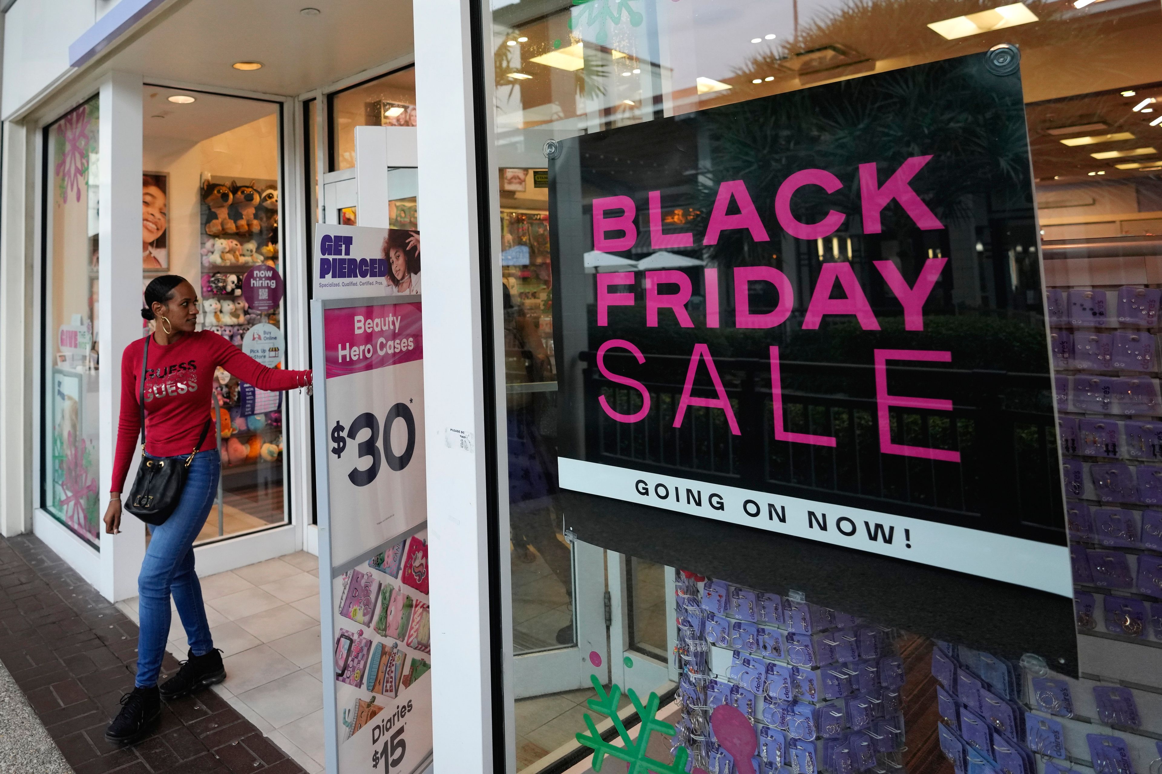 Shoppers exit a Claire's accessories store advertising sales ahead of Black Friday and the Thanksgiving holiday, Monday, Nov. 21, 2022, in Miami. Retailers are ushering in the start of the holiday shopping season on the day after Thanksgiving, preparing for the biggest crowds since 2019. (AP Photo/Rebecca Blackwell)