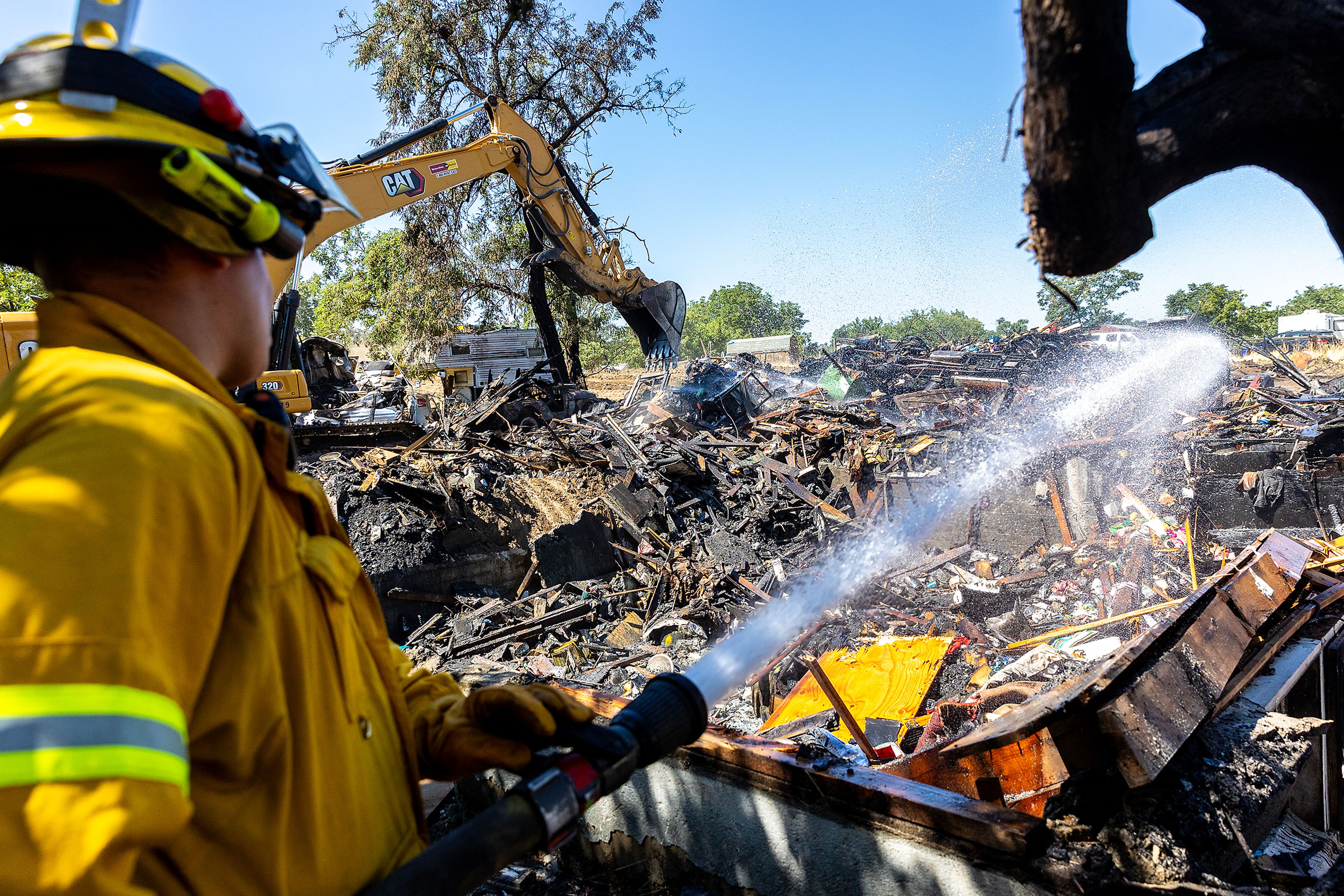 A firefighter sprays down the debris as an excavator moves it at the scene of a structure fire, caused by a firework that misfired from across the street on Thursday night, on Poplar Street Friday in Clarkston.