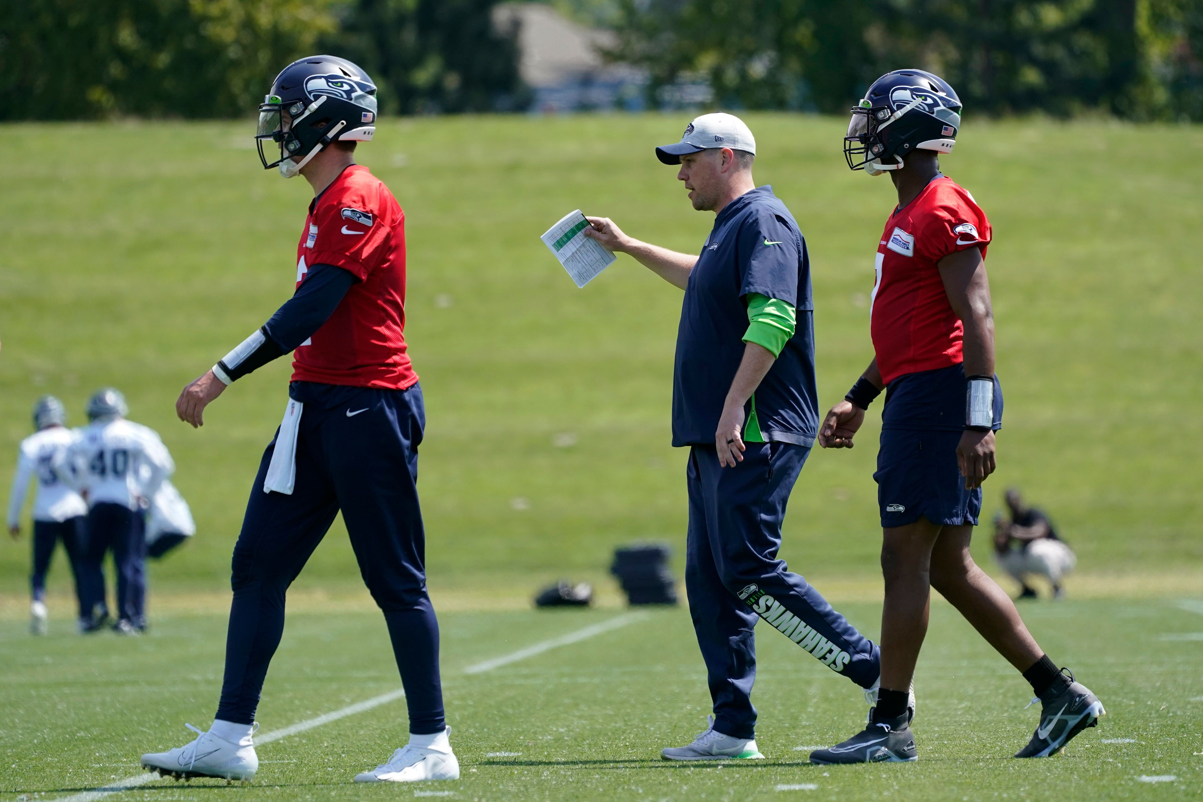 Seattle Seahawks offensive coordinator Shane Waldron, center, walks with quarterbacks Drew Lock, left, and Geno Smith, right, during NFL football practice Monday, May 23, 2022, in Renton, Wash. (AP Photo/Ted S. Warren)