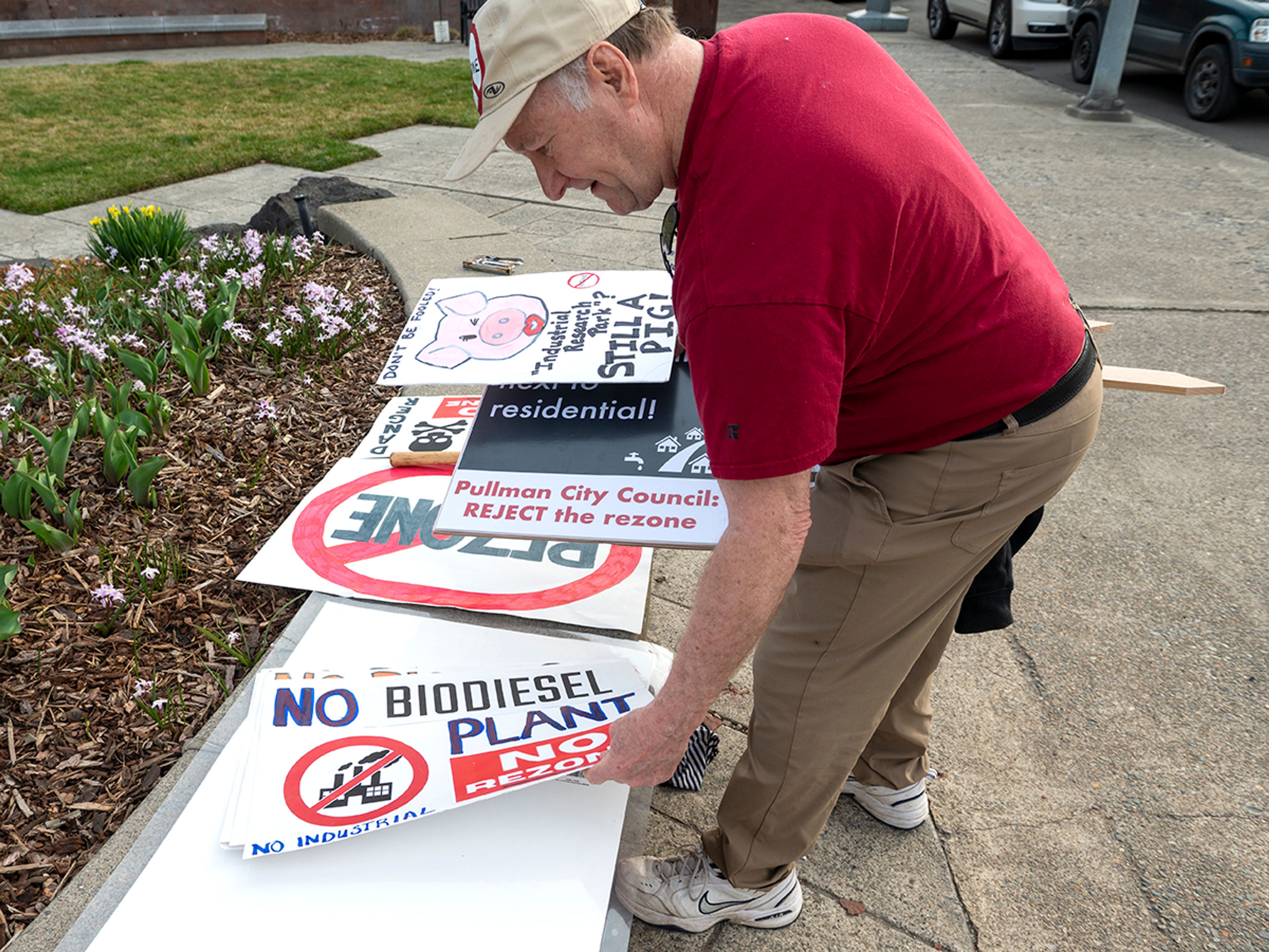 James Carr flips through signs in Cougar Plaza during a protest Monday against the Port of Whitman’s decision to rezone on a residential property next to Whispering Hills neighborhood in Pullman.