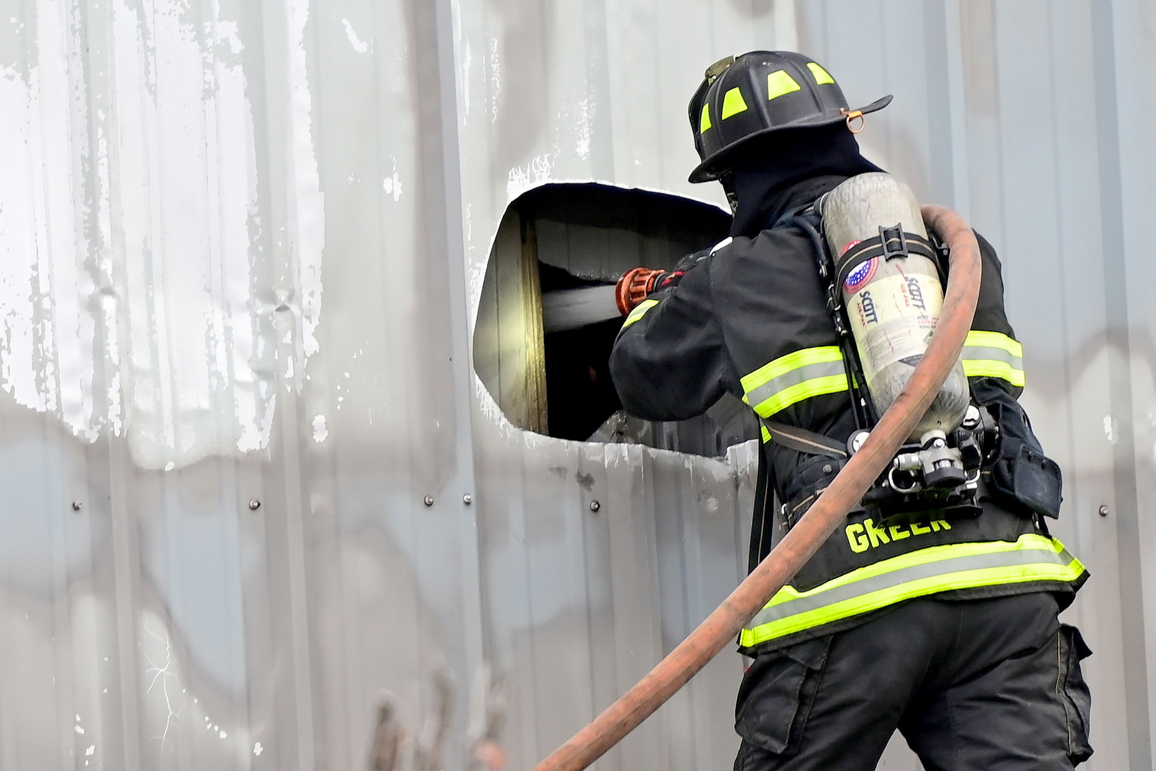 Fire crews spray through holes cut into the side of units at Express Storage in the aftermath of the large fire along Moscow-Pullman Highway on Thursday.