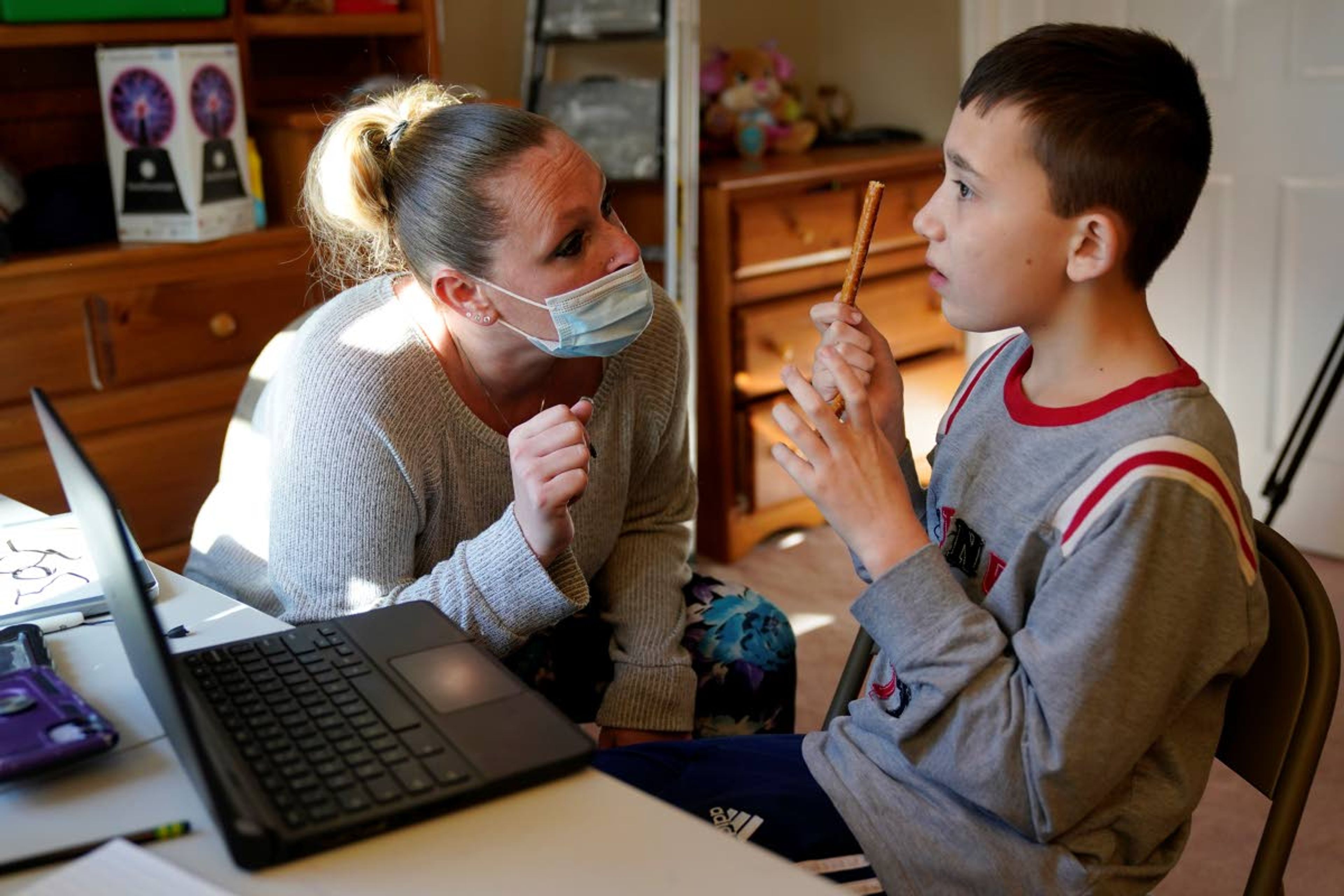 Paraprofessional Jessica Wein helps Josh Nazzaro with his classwork while attending class virtually from his home in Wharton, N.J., Wednesday, Nov. 18, 2020. Without any in-school special education services for months, Nazzaro’s normally sweet demeanor has sometimes given way to aggressive meltdowns that had been under control before the pandemic. The teenager, who has autism and is nonverbal, often wanted no part of his online group speech therapy sessions, and when he did participate, he needed constant hands-on guidance from aides hired by his family. (AP Photo/Seth Wenig)