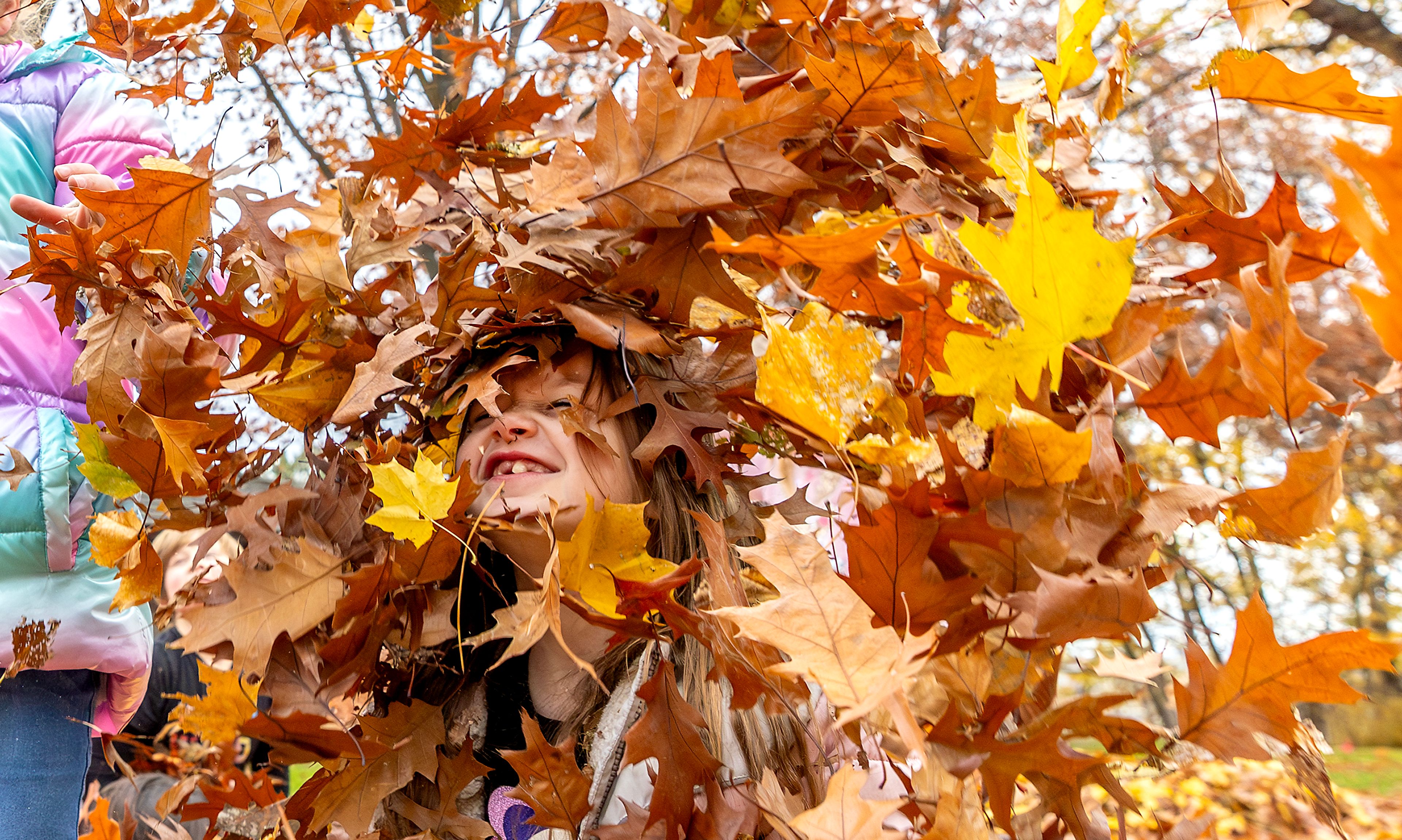 Paxley Jensen grins as leaves thrown in the air fall down around her Wednesday outside Children's House Montessori School at Pioneer Park Wednesday in Lewiston.