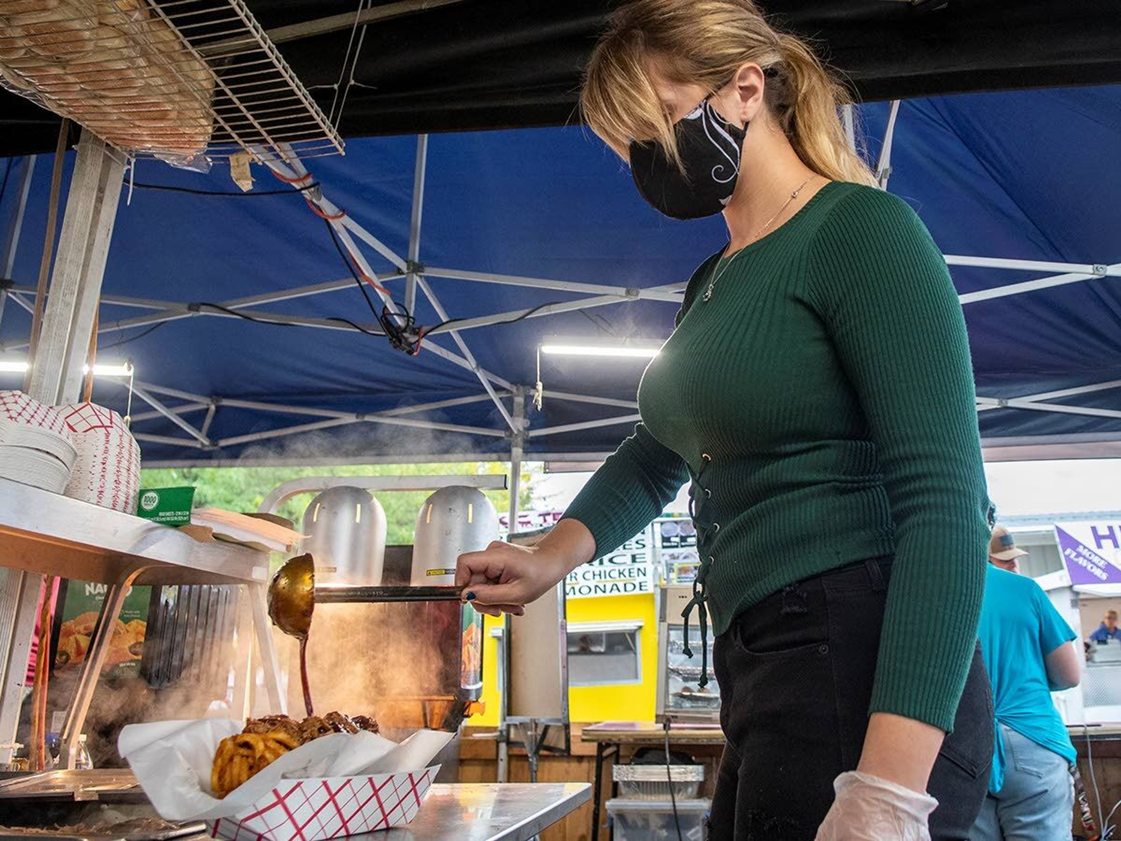 Samantha Cogswell, manager of Country Snack Shack, pours barbecue sauce over a bed of curly fries and pulled pork as she makes “Dirty Fries” for a customer at the Latah County Fair on Saturday morning in Moscow.