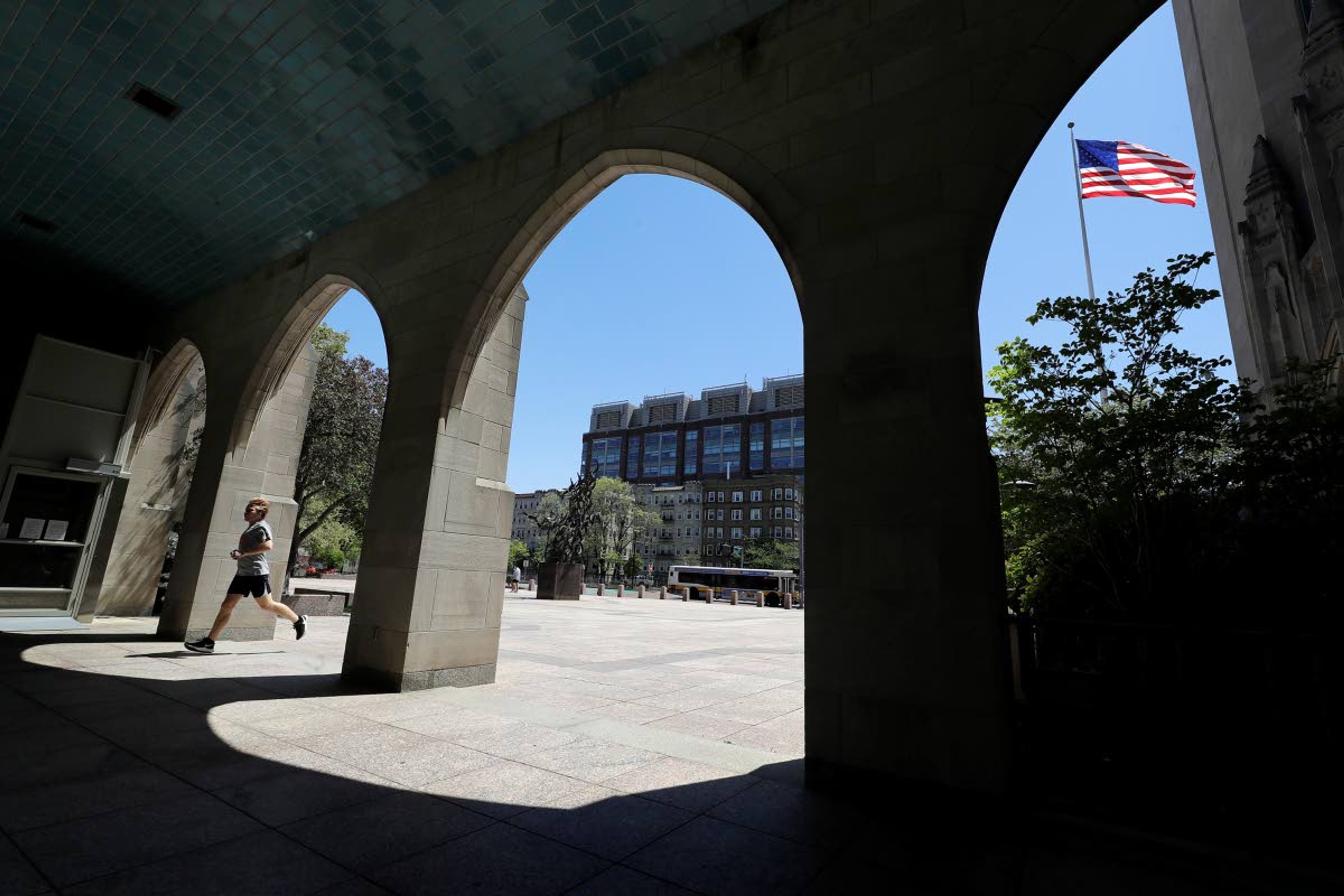 In this Wednesday, May 20, 2020 photo a runner passes through an arch on the campus of Boston University, in Boston. Boston University is among a growing number of universities making plans to bring students back to campus this fall, but with new measures meant to keep the coronavirus at bay. (AP Photo/Steven Senne)