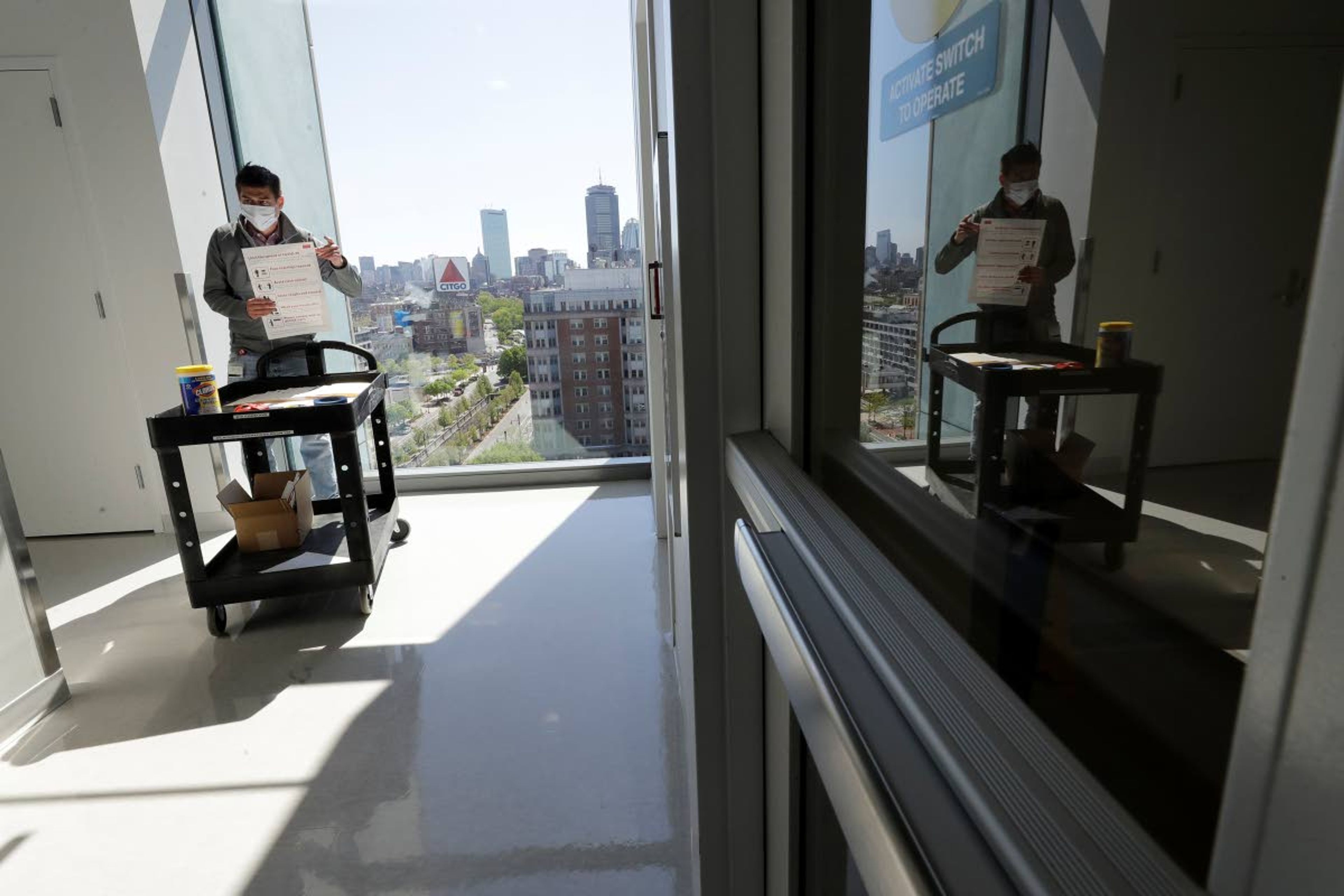 Kevin Gonzales, director of operations at the Rajen Kilachand Center for Integrated Life Sciences and Engineering, at Boston University, prepares to place safe distancing signage in a hallway on the school's campus, in Boston, Thursday, May 21, 2020. Boston University is among a growing number of universities making plans to bring students back to campus this fall, but with new measures meant to keep the coronavirus at bay. (AP Photo/Steven Senne)