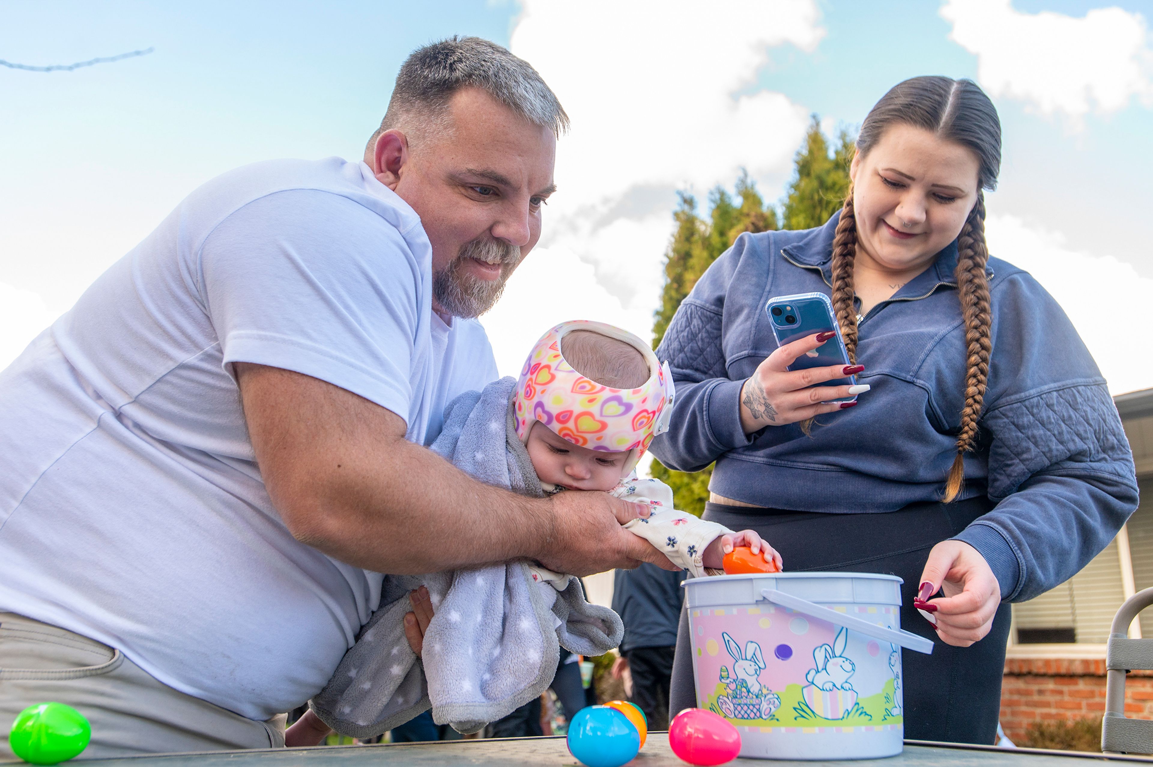 Zach Wilkinson/Daily News Destiny Meneley records as her father, Dean Richards, helps his 7-month-old granddaughter, Oaklynn Meneley, place plastic eggs into a basket Friday during the annual Easter egg hunt at Aspen Park of Cascadia in Moscow.