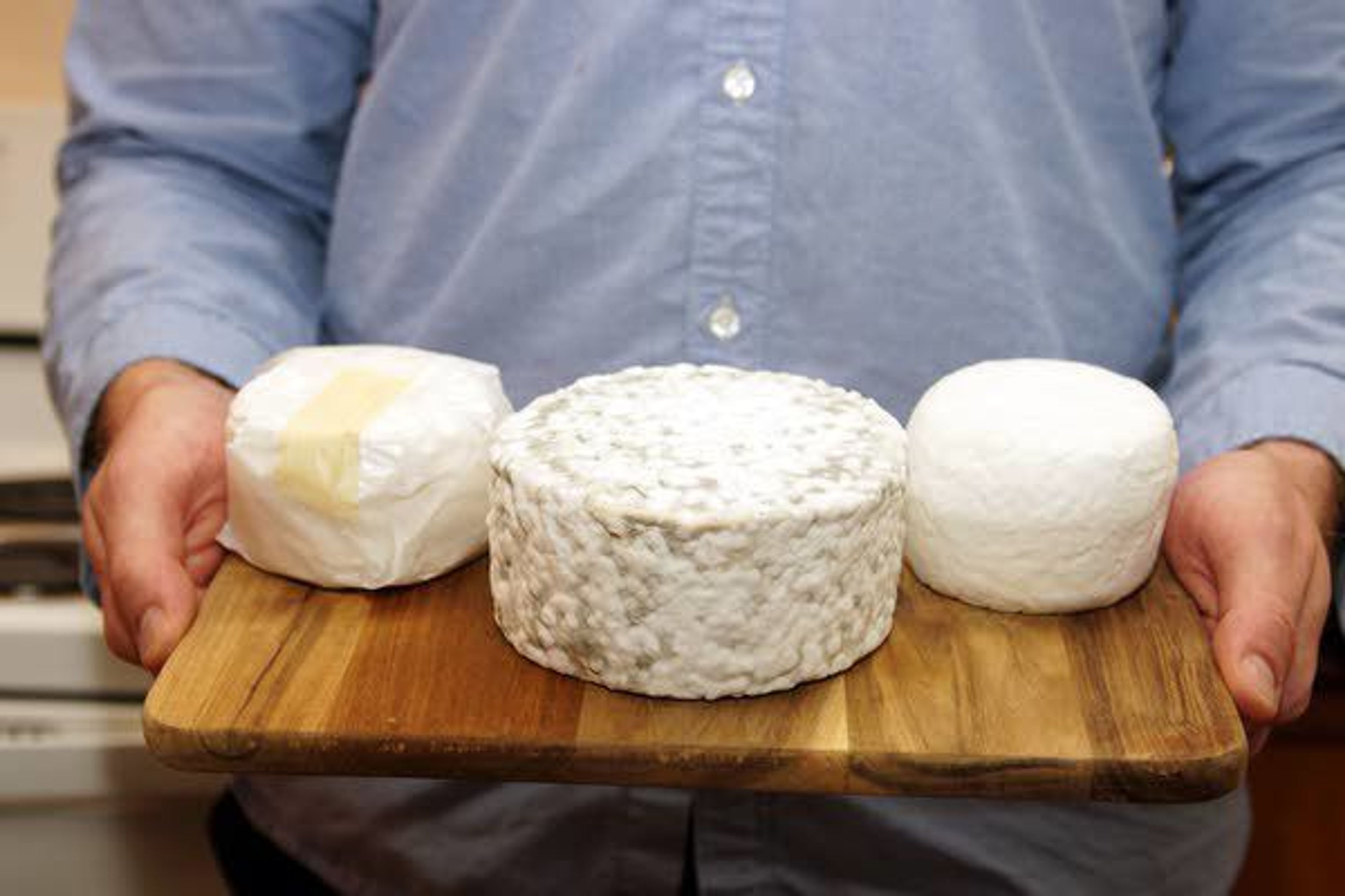 Jobe Ritchie holds a board with some of the cheese he has made, including two small blocks of buttermilk brie, one wrapped in waxed paper, and a larger one that was supposed to be a blue cheese but was accidently contaminated with a brie culture.