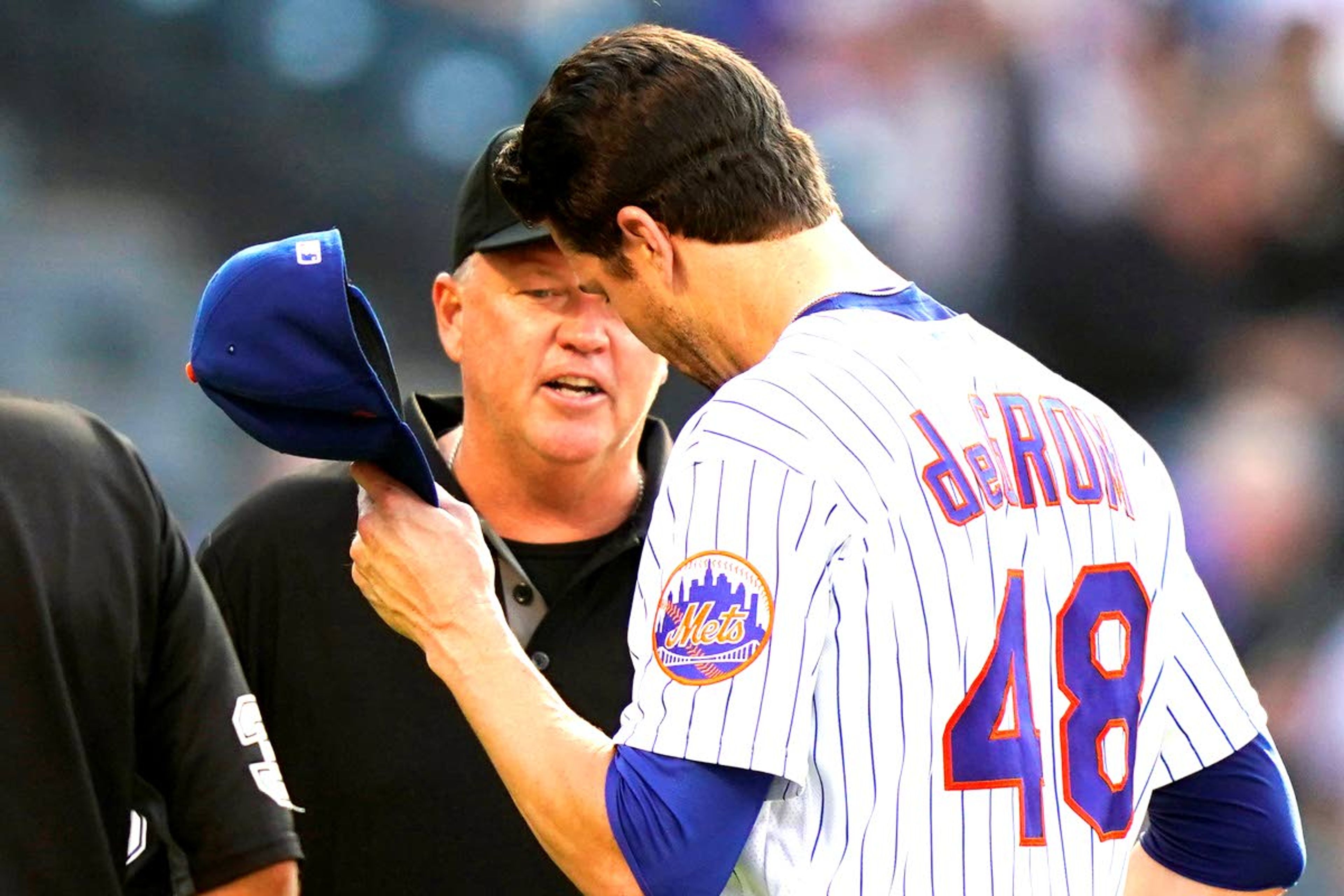 Third base umpire Ron Kulpa, left, looks inside the cap of New York Mets starting pitcher Jacob deGrom (48) after deGrom pitched in the top of the fifth inning of a baseball game against the Atlanta Braves, Monday, June 21, 2021, in New York. (AP Photo/Kathy Willens)