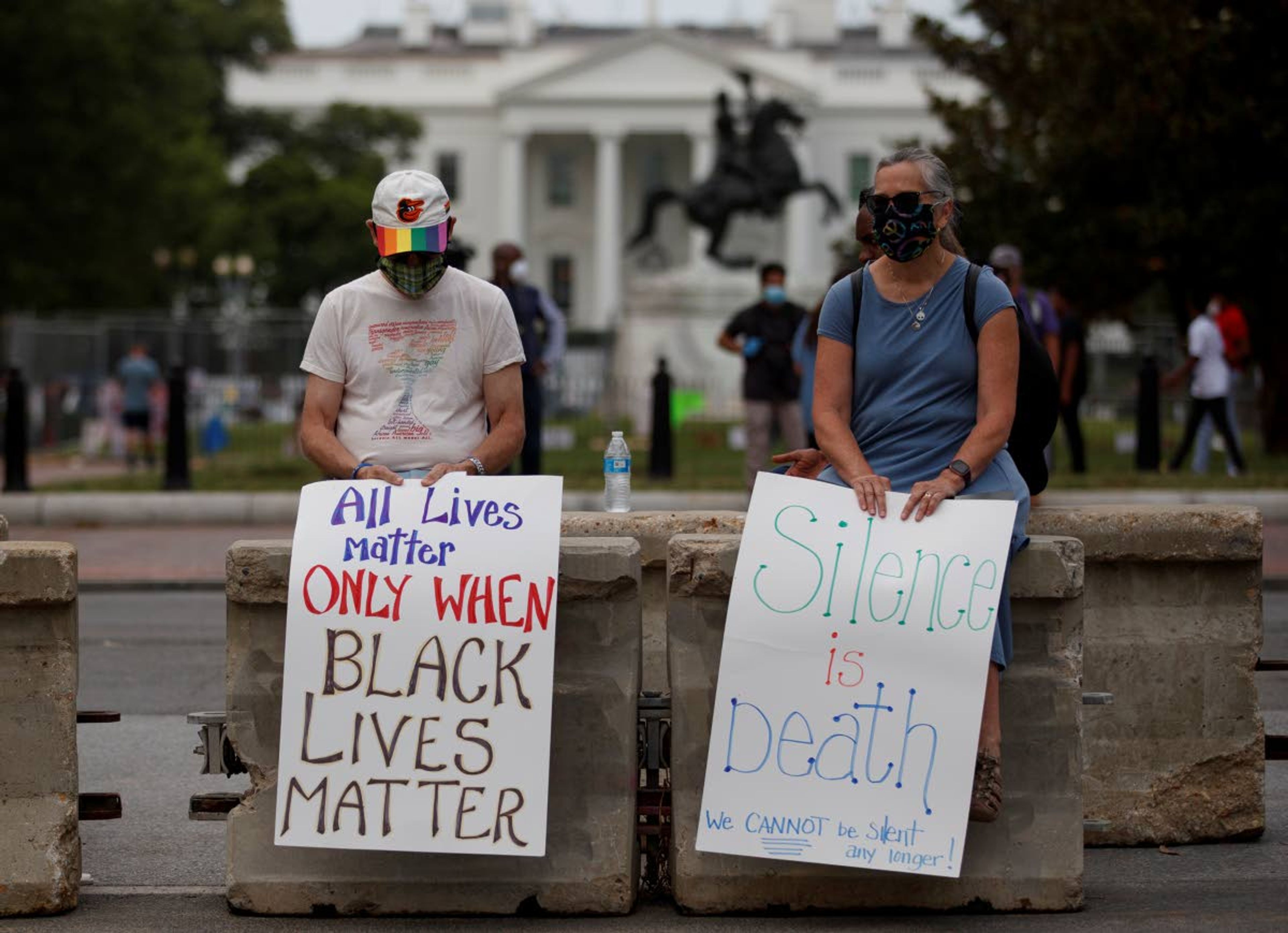 Rick and Jayna Powell sit on a concrete barricade with signs the read "All Lives Matter Only When Black Lives Matter" and 'Silence is Death We Cannot be Silent Any Longer!" Friday, June 19, 2020, in Washington, as the White House is seen behind them. (AP Photo/Carolyn Kaster)