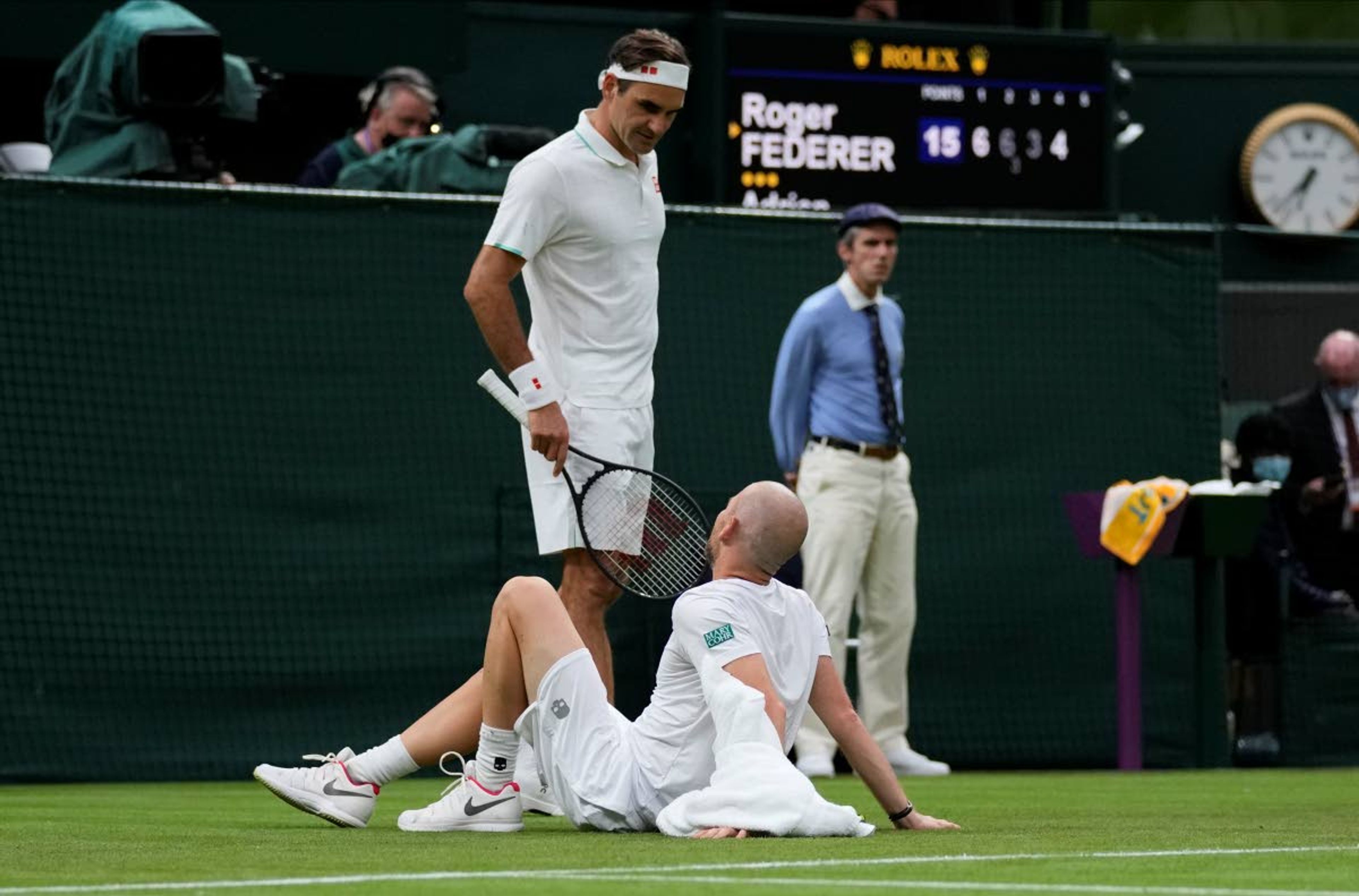 Switzerland's Roger Federer talks to Adrian Mannarino of France as he lies on the ground in pain during the men's singles first round match against on day two of the Wimbledon Tennis Championships in London, Tuesday June 29, 2021. (AP Photo/Kirsty Wigglesworth)