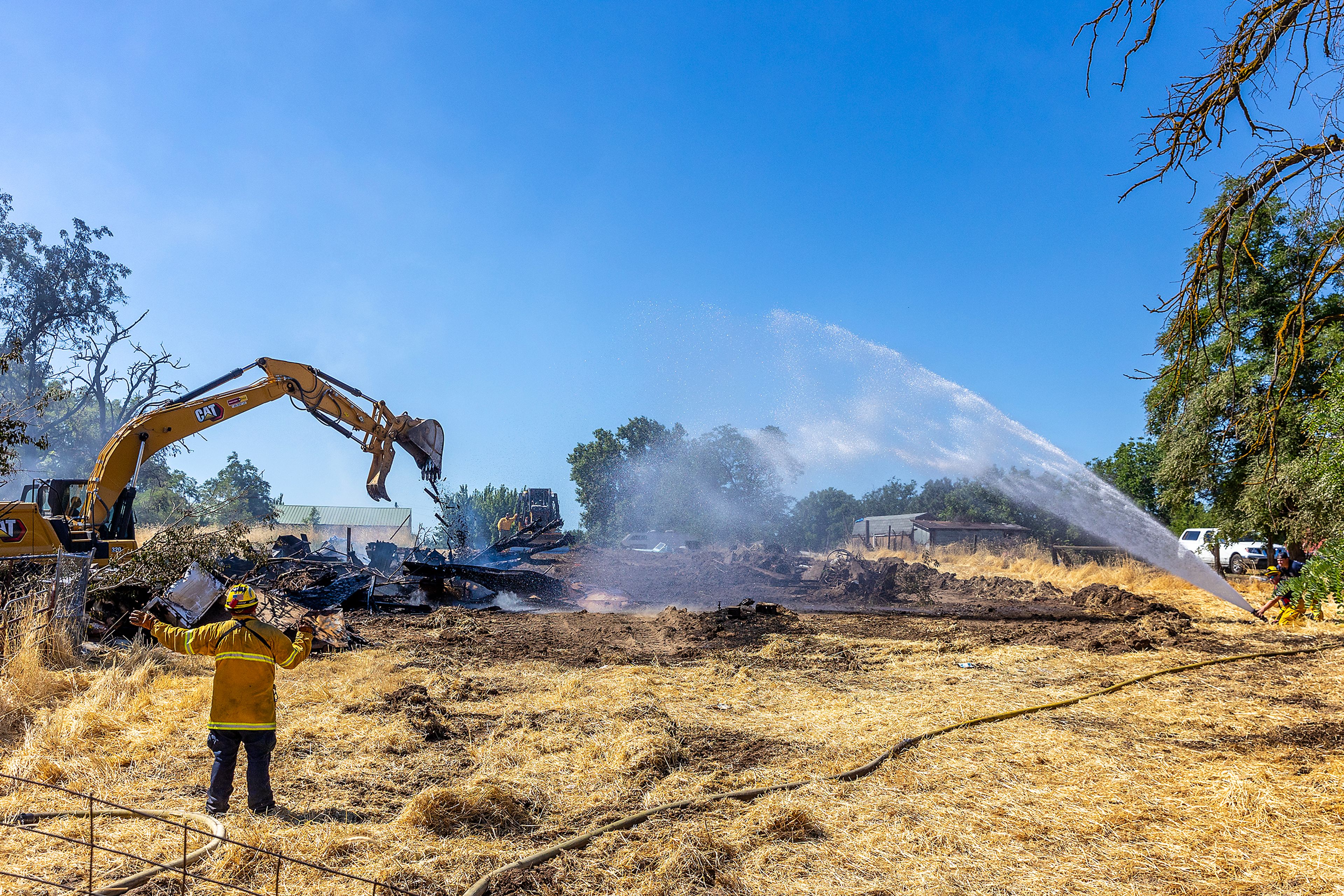 Firefighters spray down the remnants of a structure fire as a excavator moves debris to get to parts of the fire still smoking Friday in Clarkston.