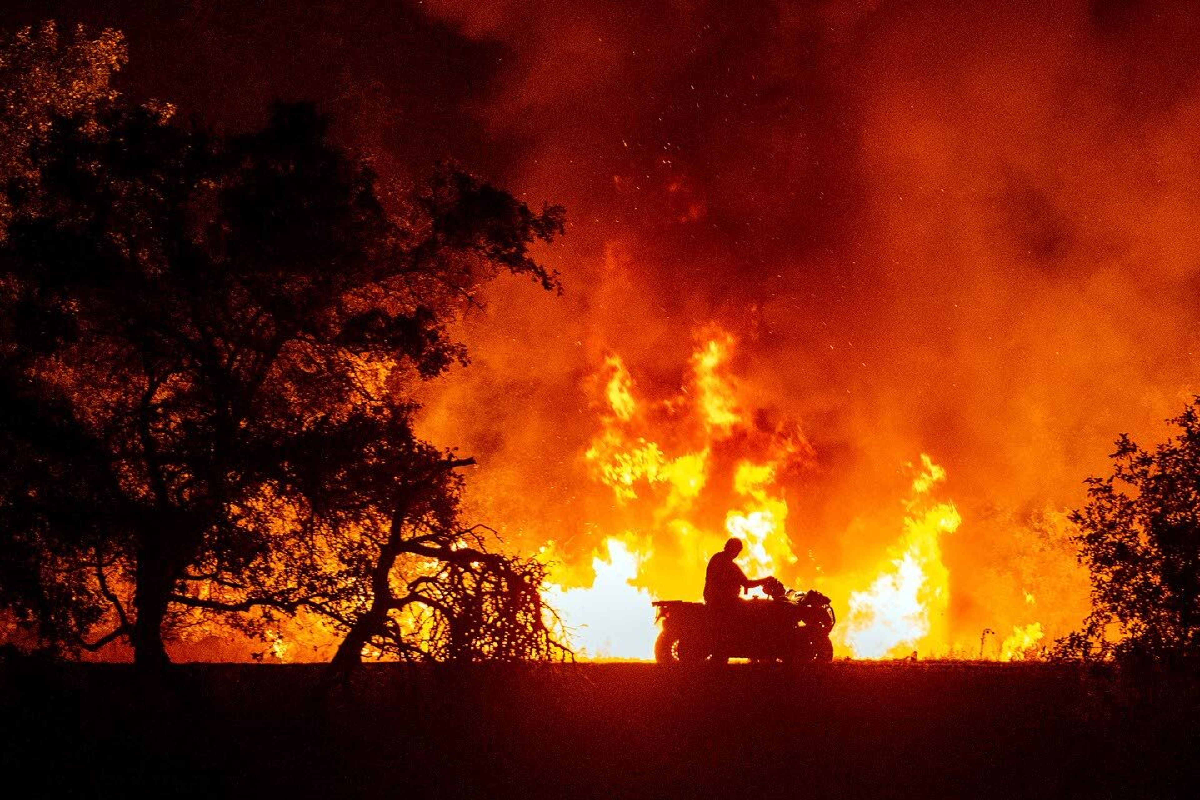 A man driving a four-wheeler maneuvers past large flames from the Snake River Complex fire that reached the bottom of the canyon just south of Buffalo Eddy on Friday night, as seen from across the river on Snake River Road.