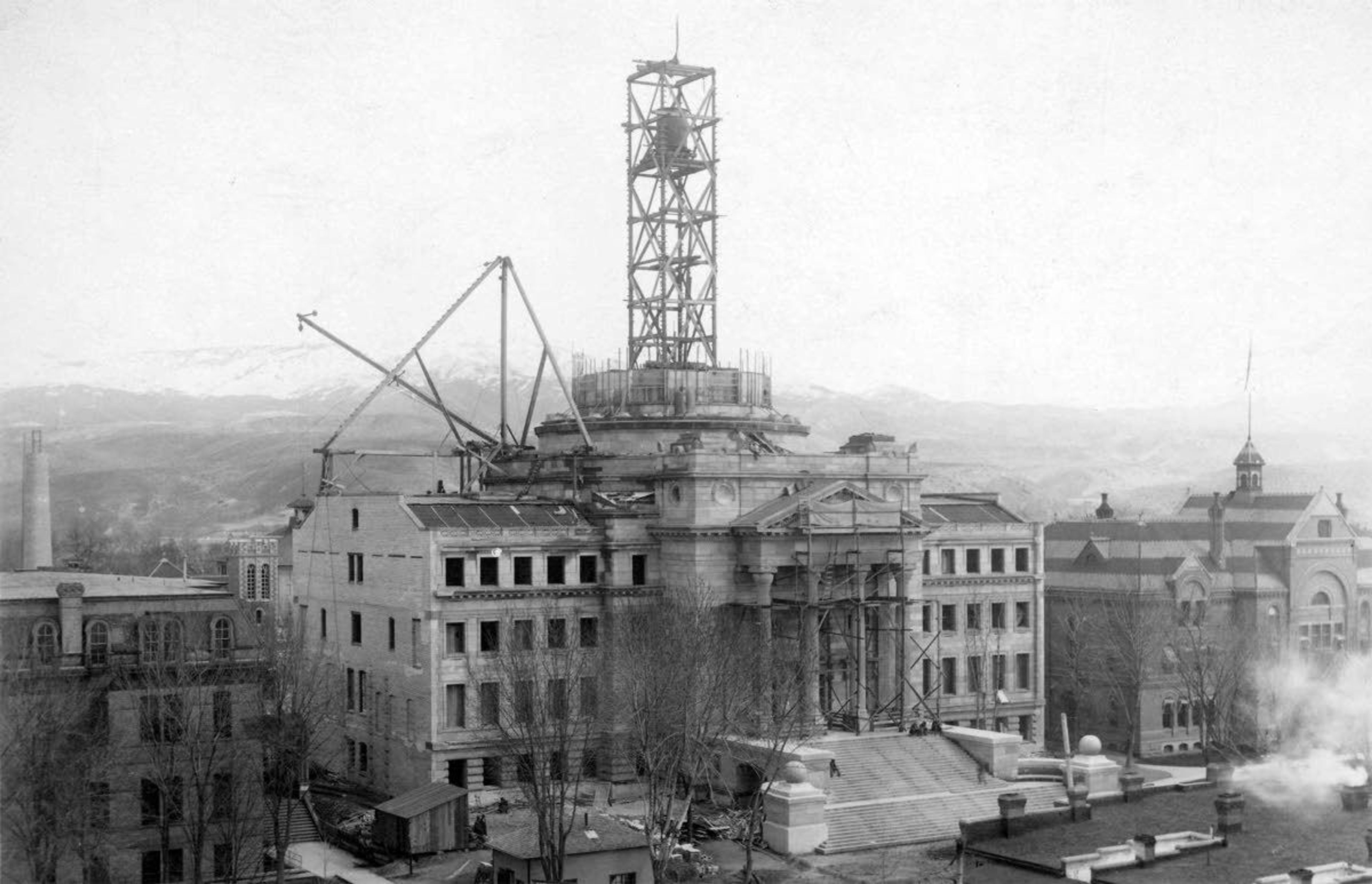 The Idaho State Capitol is seen under construction in 1912. On the left is the Central School — the first school built by the Independent School District of Boise City No. 1 — while the Territorial Capitol stands on the right. The school and Territorial Capitol building were torn down after the completion of the new building.