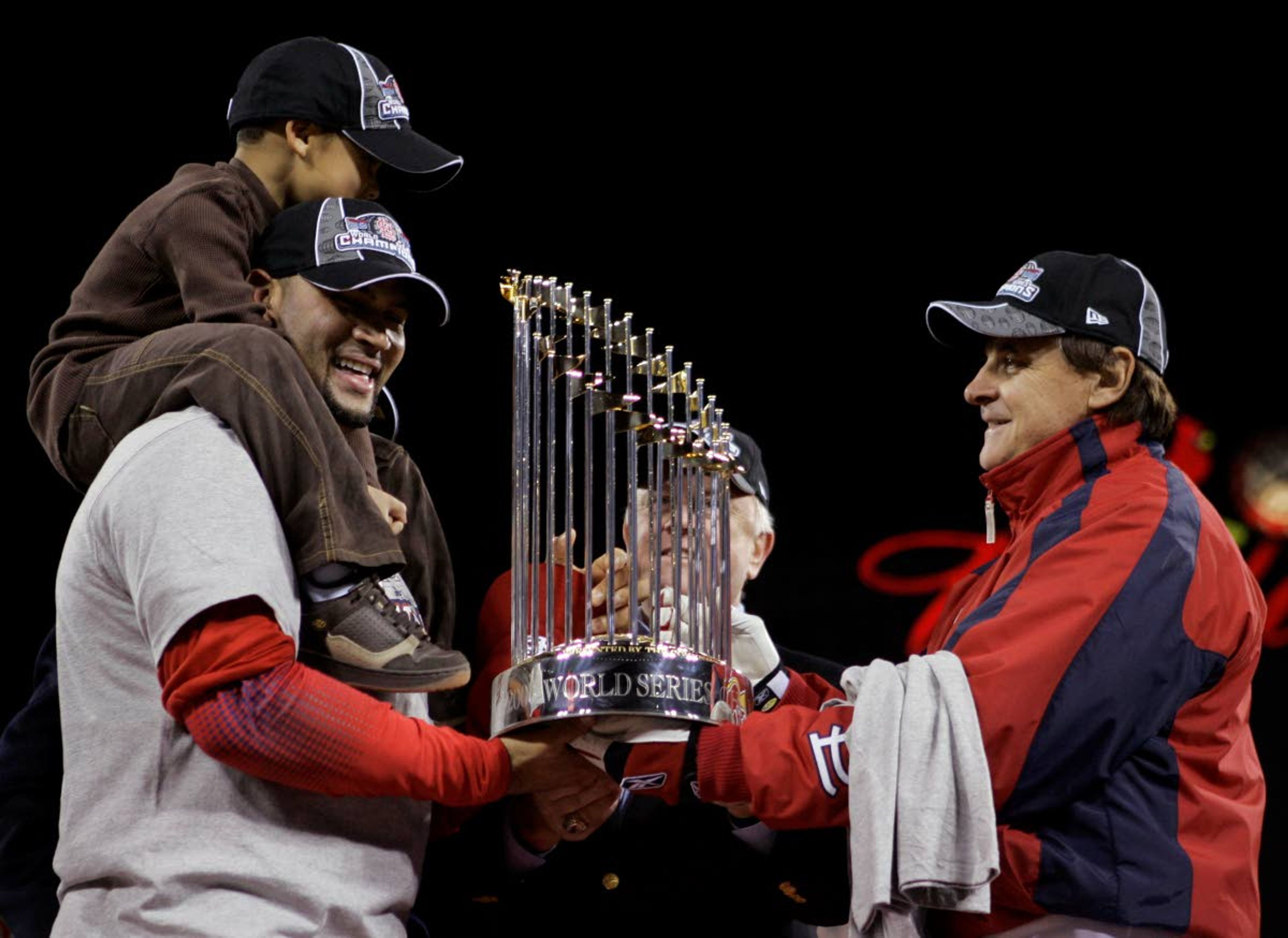 FILE - St. Louis Cardinals first baseman Albert Pujols, with his son A.J. Alberto Jr. on his shoulders, holds onto the World Series trophy with Cardinals manager Tony La Russa, right and General Manager Walt Jocketty, second right, after winning Game 5 of the World Series against the Detroit Tigers in St. Louis, in this Friday, Oct. 27, 2006, file photo. Pujols has been designated for assignment by the Los Angeles Angels, abruptly ending the 41-year-old superstar slugger's decade with his second major league team. The Angels announced the move Thursday, May 6, 2021, a day after Pujols wasn't in their lineup for their fourth consecutive loss. (AP Photo/Elise Amendola, File)