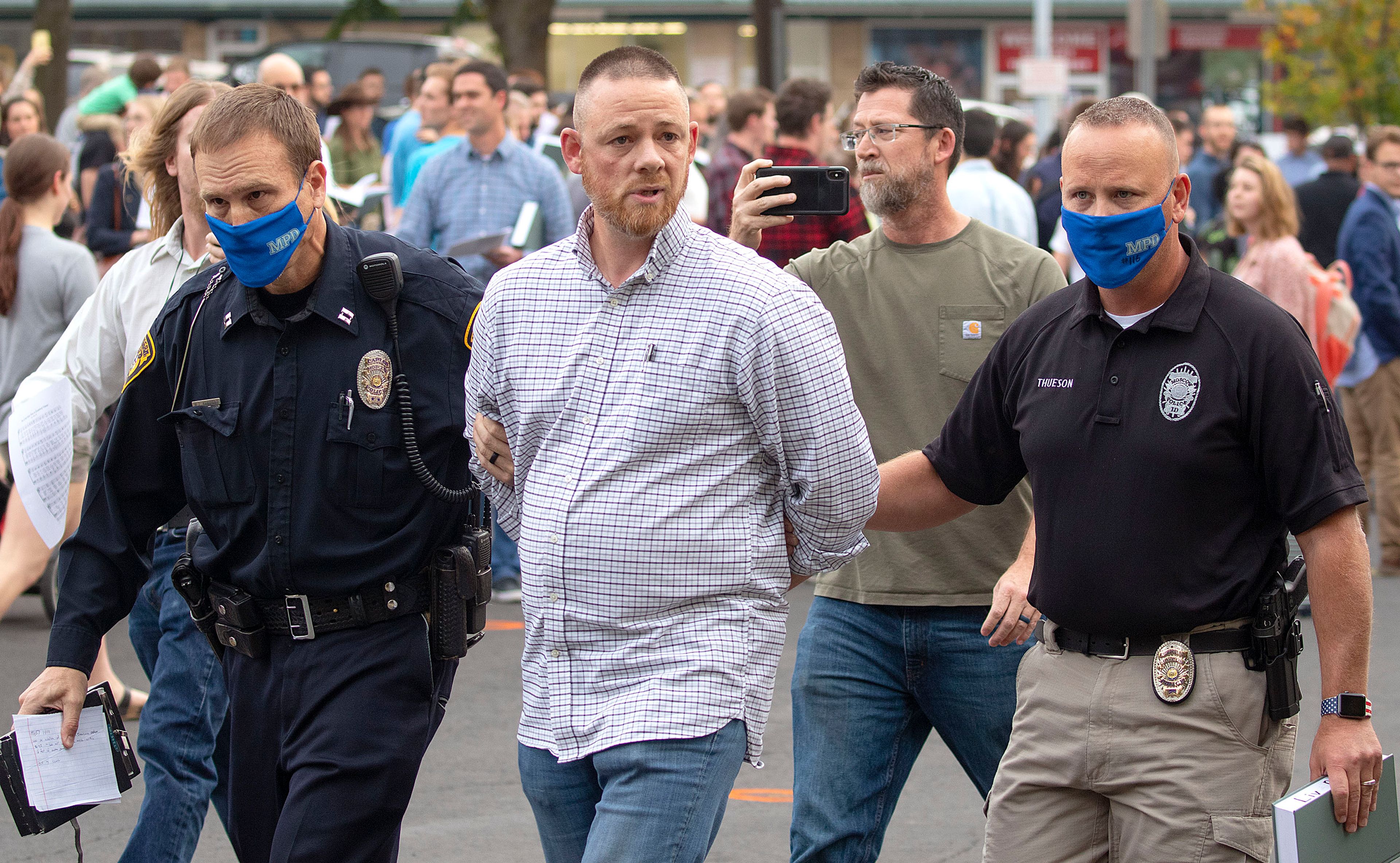 Gabe Rench, center, is escorted to a patrol car after being arrested during a "flash psalm sing" organized by Christ Church on Wednesday outside Moscow City Hall. Rench is running against Tom Lamar for a seat on the Latah County Commission.