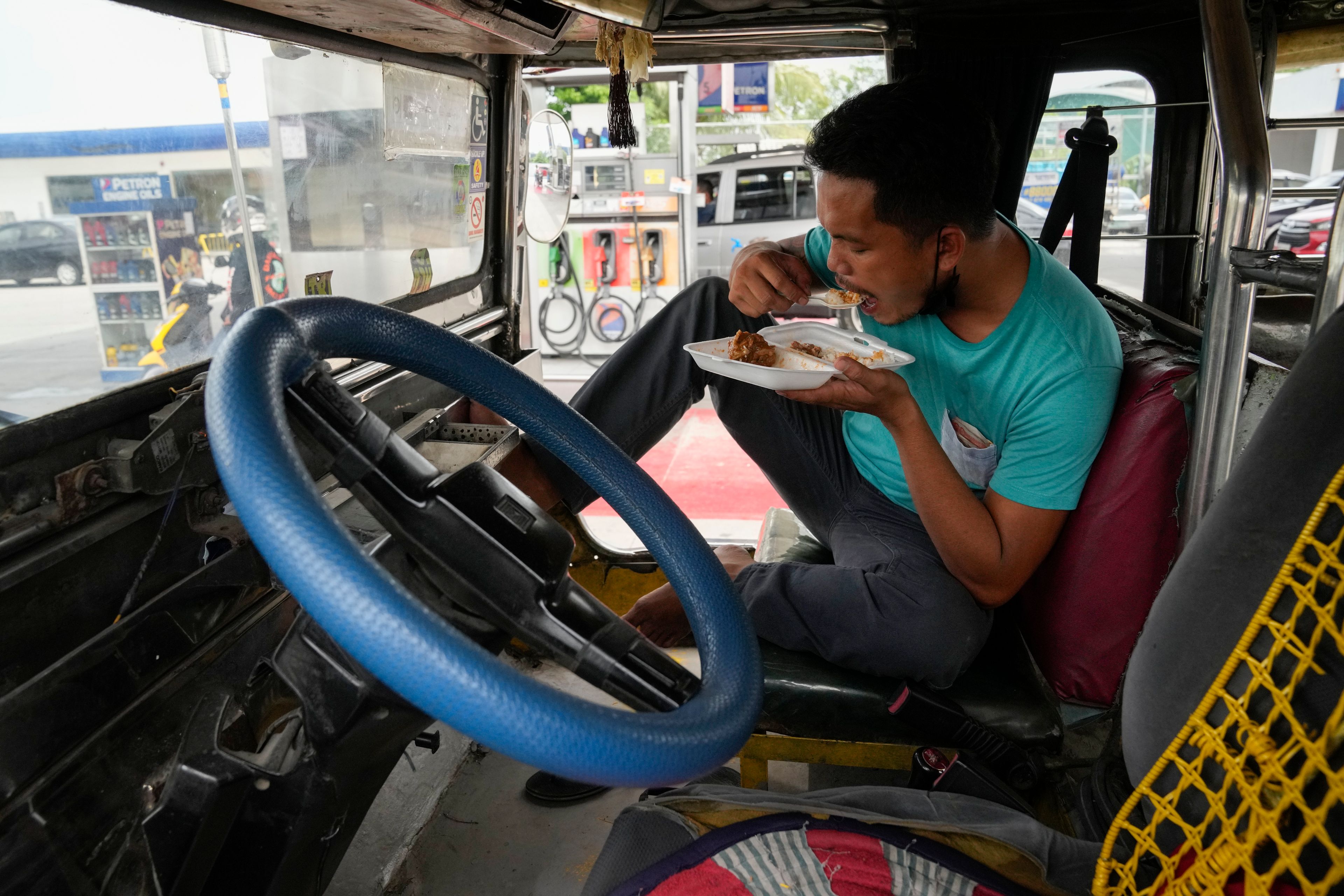 Passenger jeepney driver, Jet Marty dela Cruz, eats lunch inside his vehicle to save fuel instead of heading home as he takes a break at a gasoline station in Quezon City, Philippines on Monday, June 20, 2022. Around the world, drivers are looking at numbers on the gas pump and rethinking their habits and finances. (AP Photo/Aaron Favila)