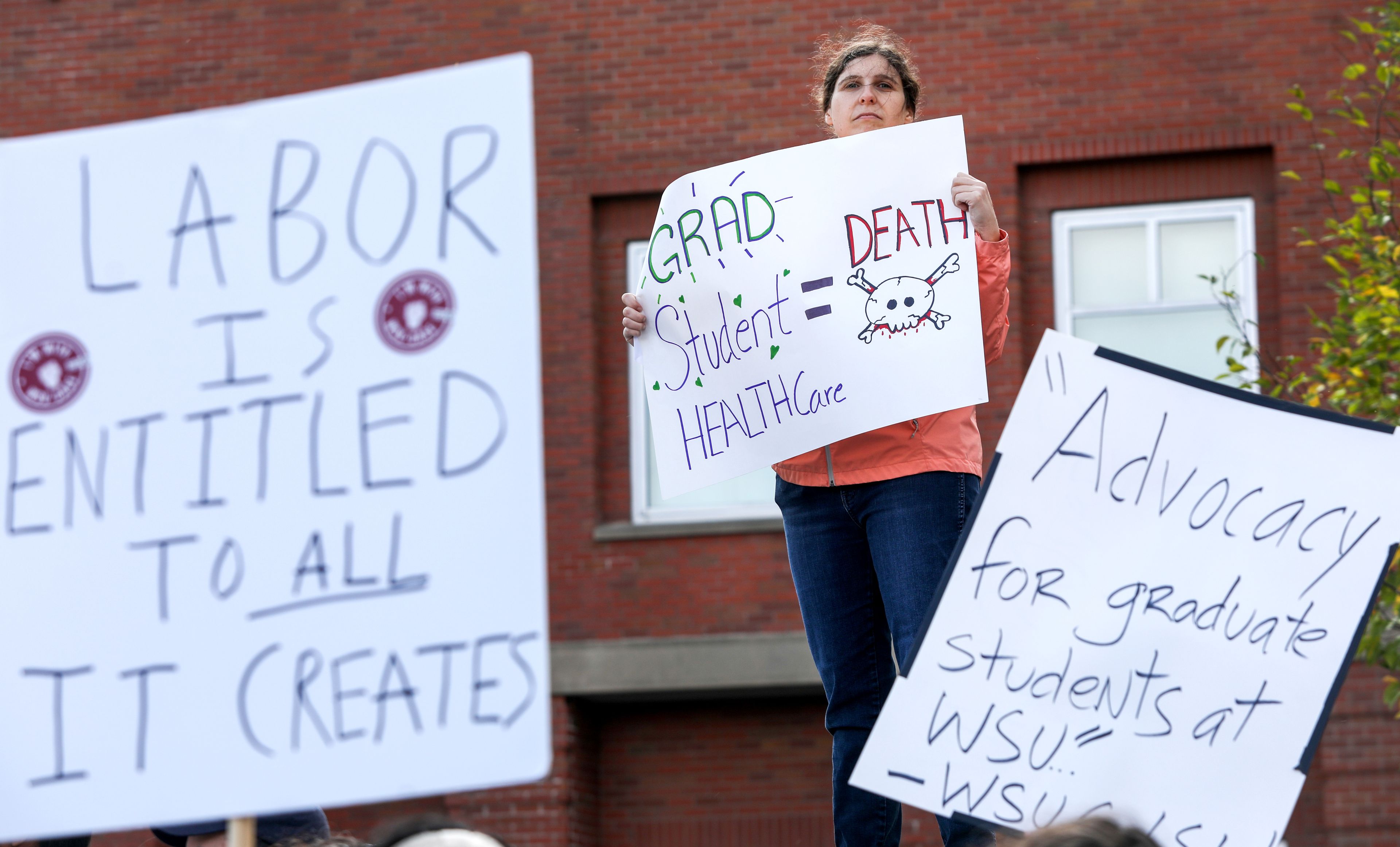 Lexi Menth, a masters student in entomology at Washington State University, stands on a wall above fellow students at a rally supporting contract negotiations for Academic Student Employees at Glenn Terrell Mall on Wednesday in Pullman.