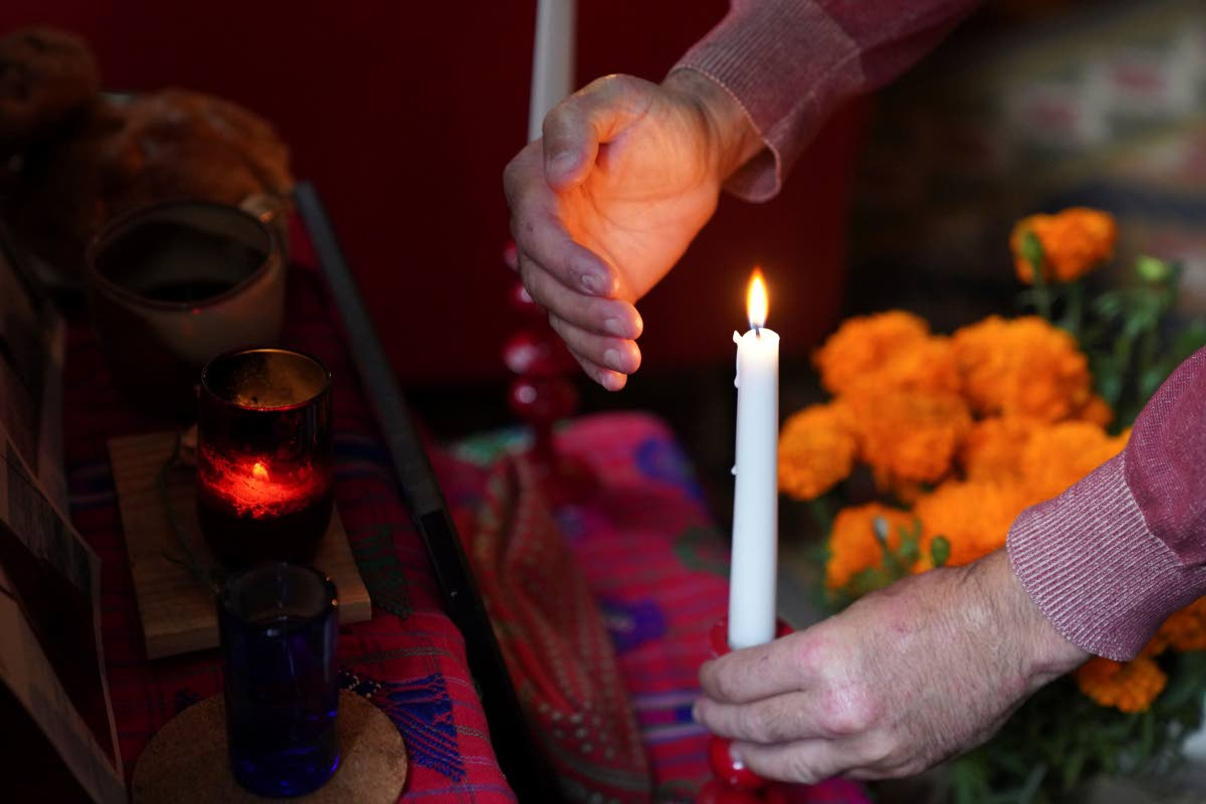 Sebastian Diaz Aguirre steadies a candle in an altar dedicated to his father, who died in a nursing home in Mexico last month, for Day of the Dead in his home in the Brooklyn borough of New York, Wednesday, Oct. 28, 2020. "He didn't die of COVID, but me and my brother said the same exact thing, that it was the pandemic that killed him," said Diaz Aguirre. (AP Photo/Emily Leshner)