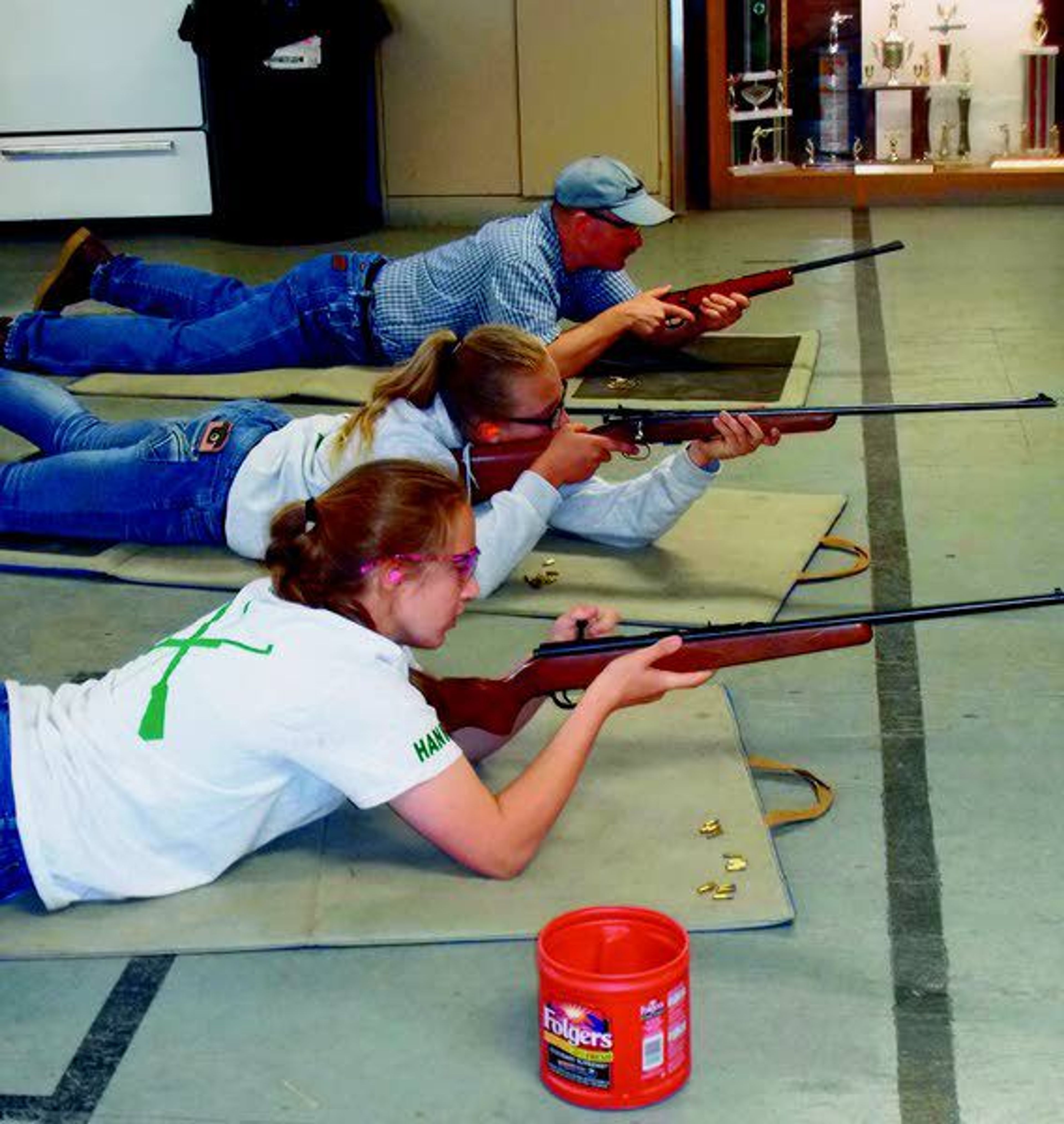 Hannah Barnes, foreground, and Kassi Schultz, center, shoot .22 air rifles during a practice for the Latah County 4-H shooting sports program Sunday at the Troy-Deary Gun Club. Scott Barnes is the man in the background providing coaching advice.