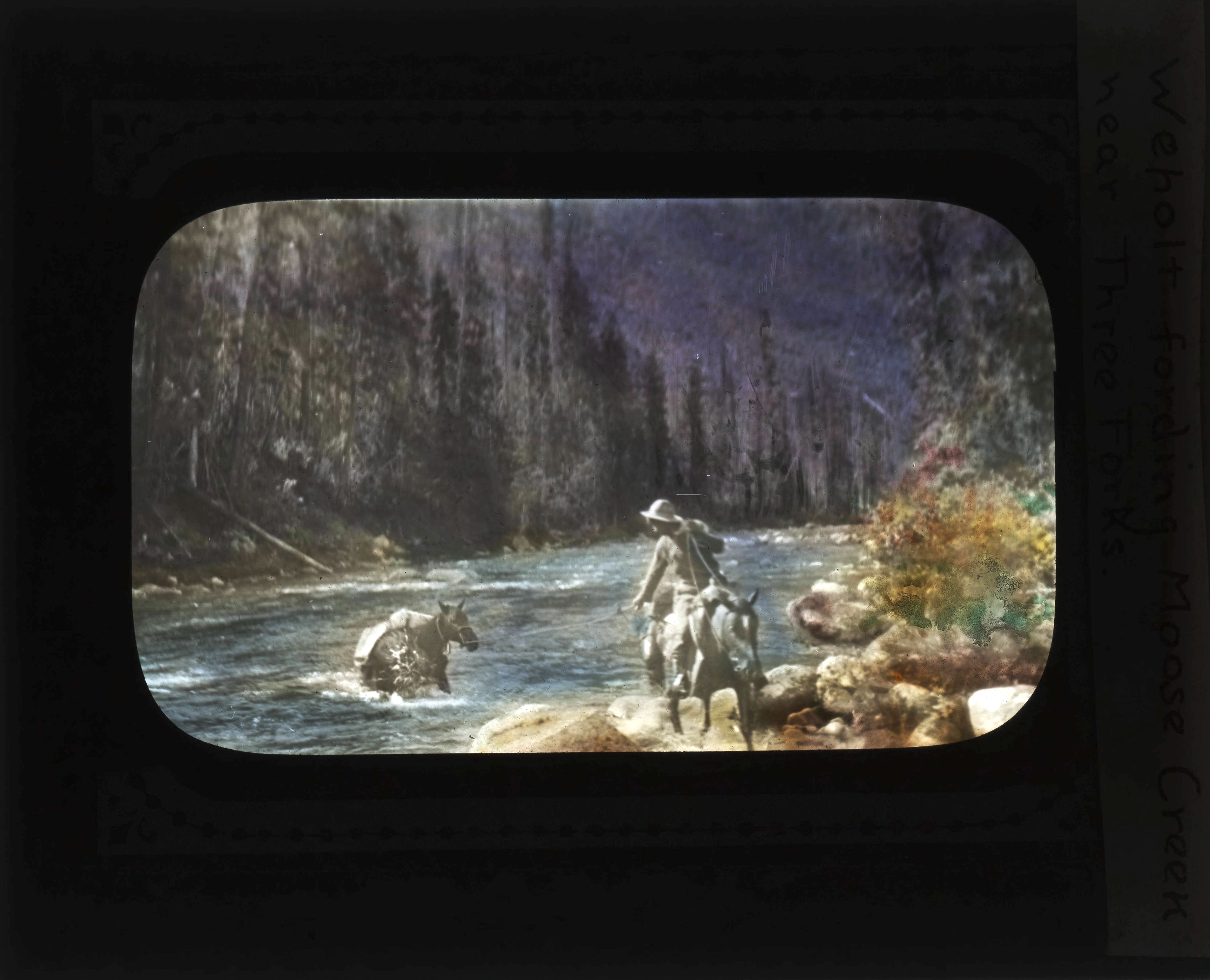 Slide label reads “Welholt fording Moose Creek near Three Forks.” Glass slides, like photography of the era, were only produced in black and white. The color would have been painted on after developing the negative.