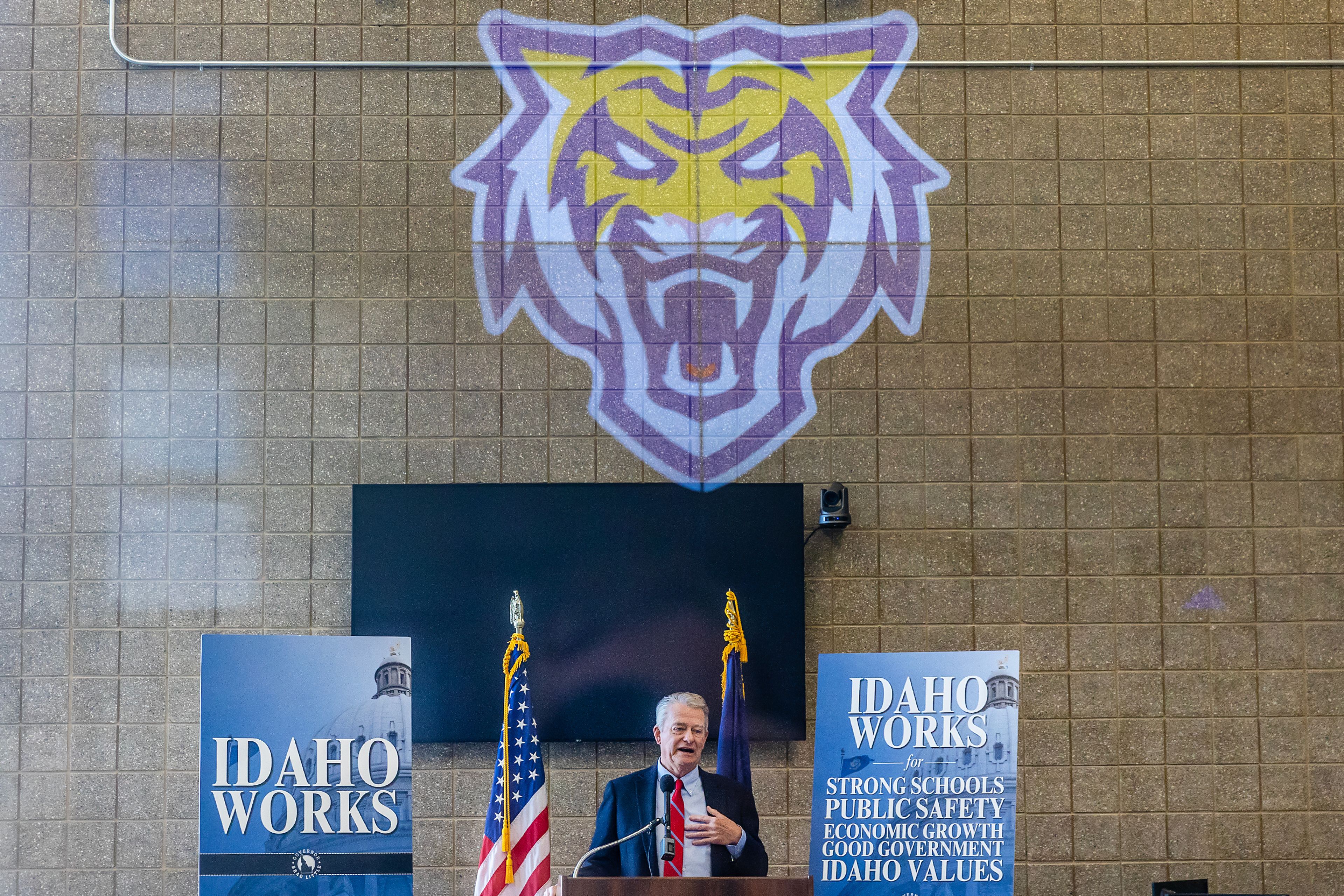 A bengal graphic is reflected across a window as Governor Brad Little speaks Wednesday at the DeAtley Center at Lewiston High School.