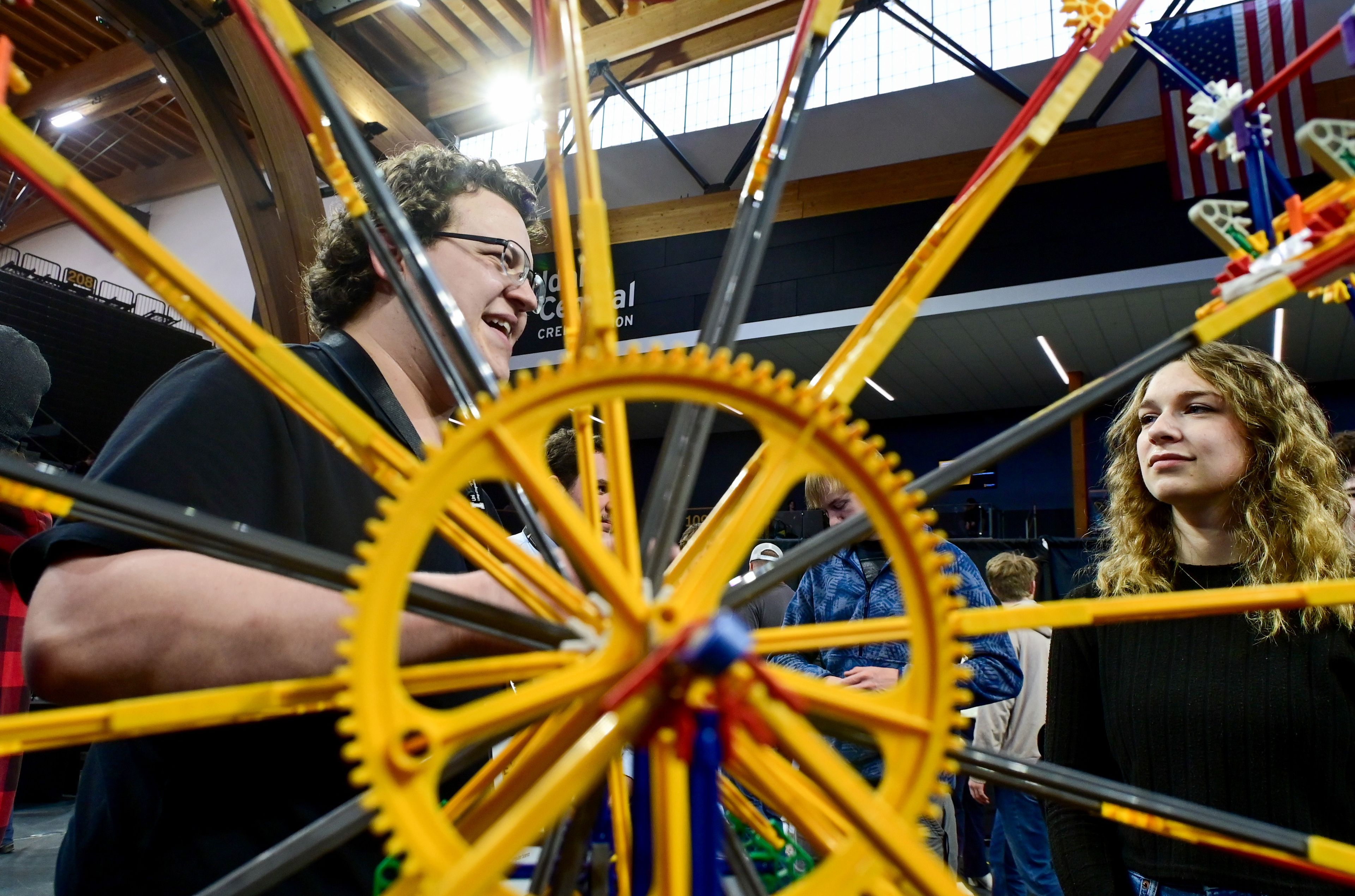 Hunter Squires, left, a senior cyber security student at the University of Idaho, is visible through the movement of a Ferris wheel model while sharing about a capstone project about modeling cybersecurity threats with a Ferris wheel to UI junior mechanical engineering major Alyssa Taylor at the Engineering Design EXPO on Friday in Moscow.