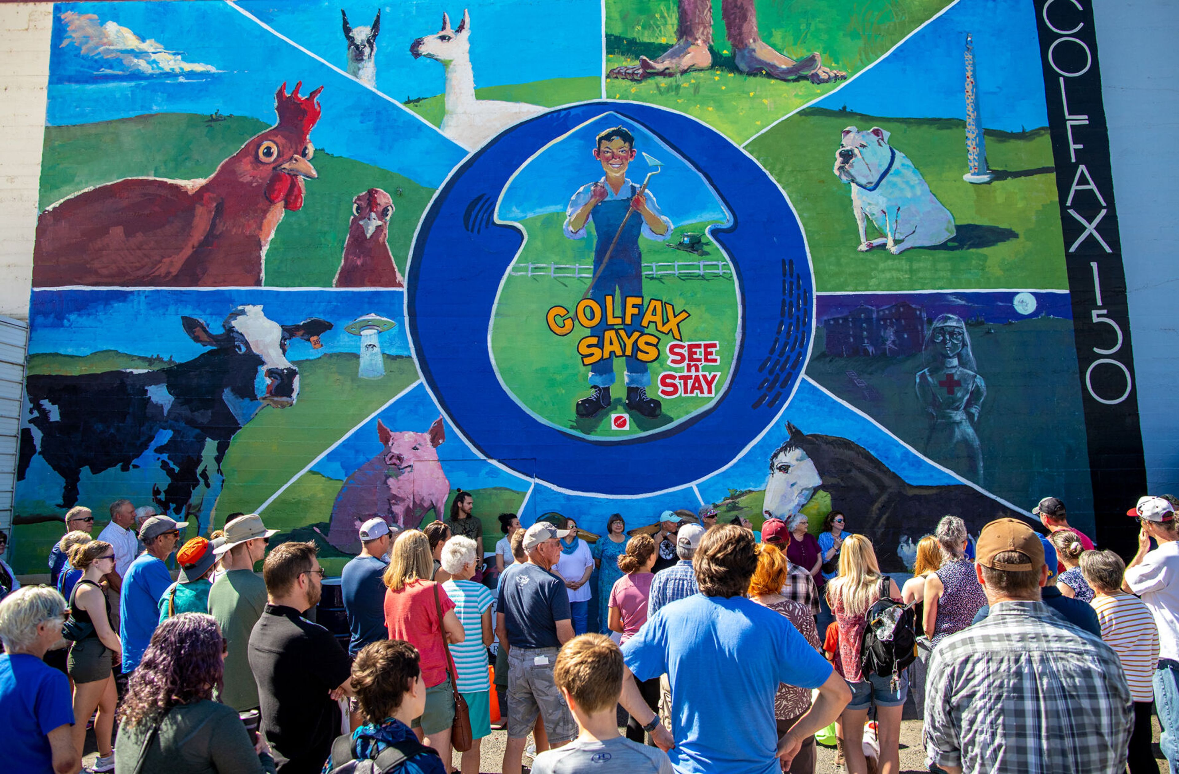 People gather around a new mural near Main Street in Colfax by local artist Henry Stinson on Saturday during the city’s 150th birthday celebration.